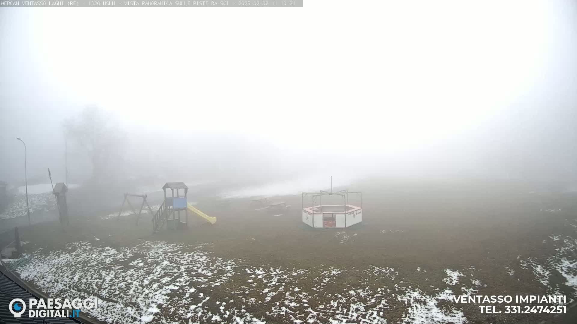 A foggy playground with a slide and other play equipment is partially covered in snow.