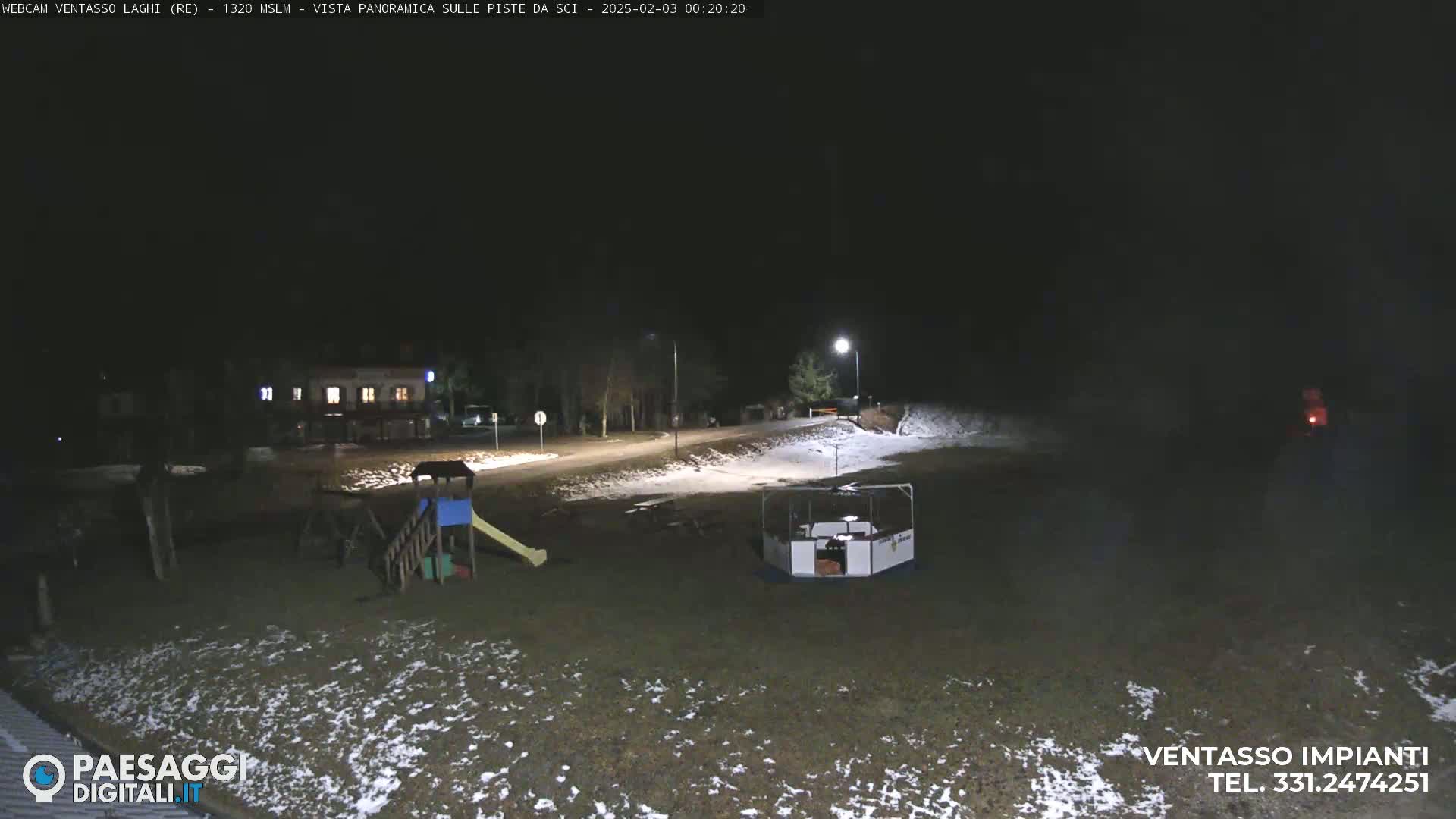 A nighttime view of a snow-dusted playground and road, illuminated by artificial lights.