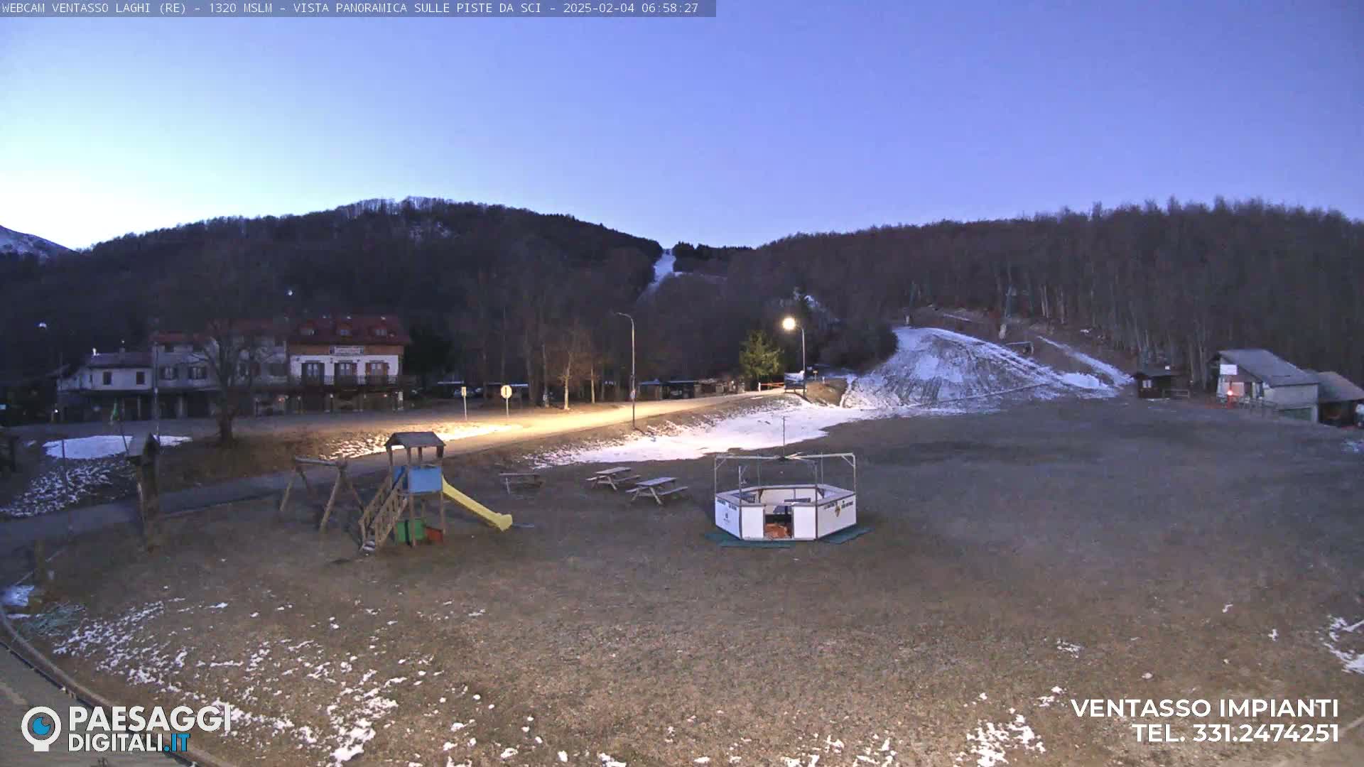 A playground with a slide and other equipment sits in a sparsely populated area near a ski slope under a twilight sky.