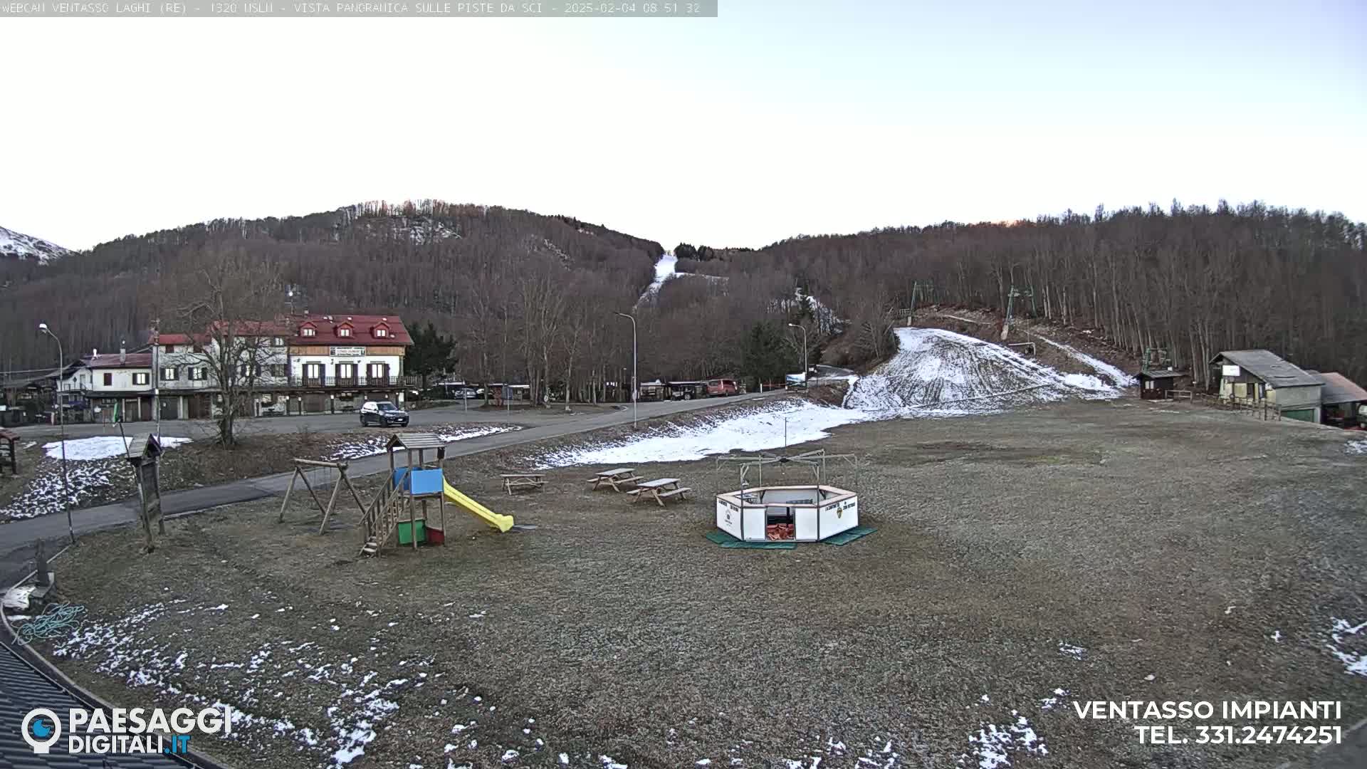 A mostly clear day shows a ski slope with patches of snow, a small village with buildings, and a playground area with a slide and swings.