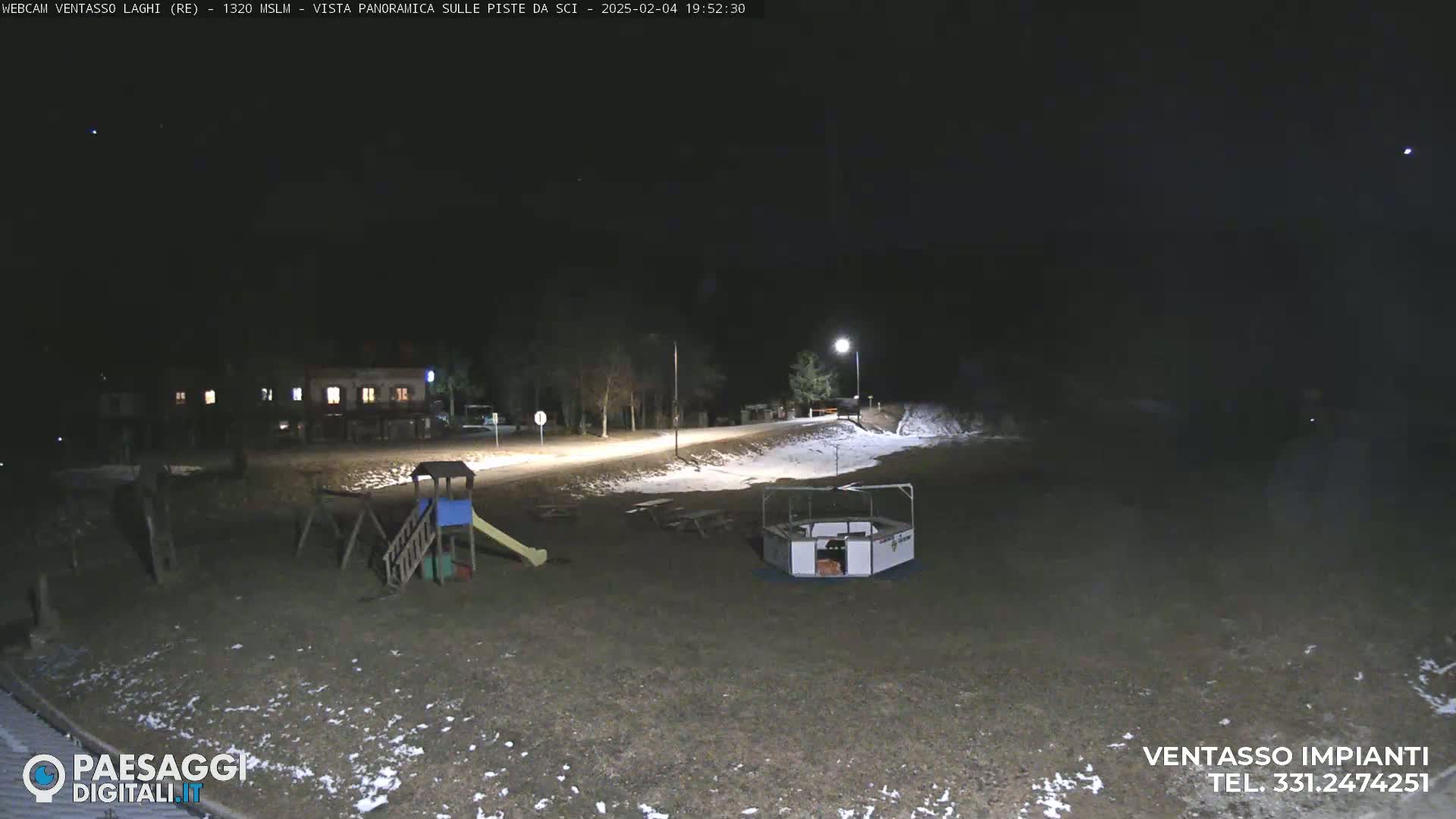 A nighttime view of a playground and a building, lightly dusted with snow, under a clear, dark sky.
