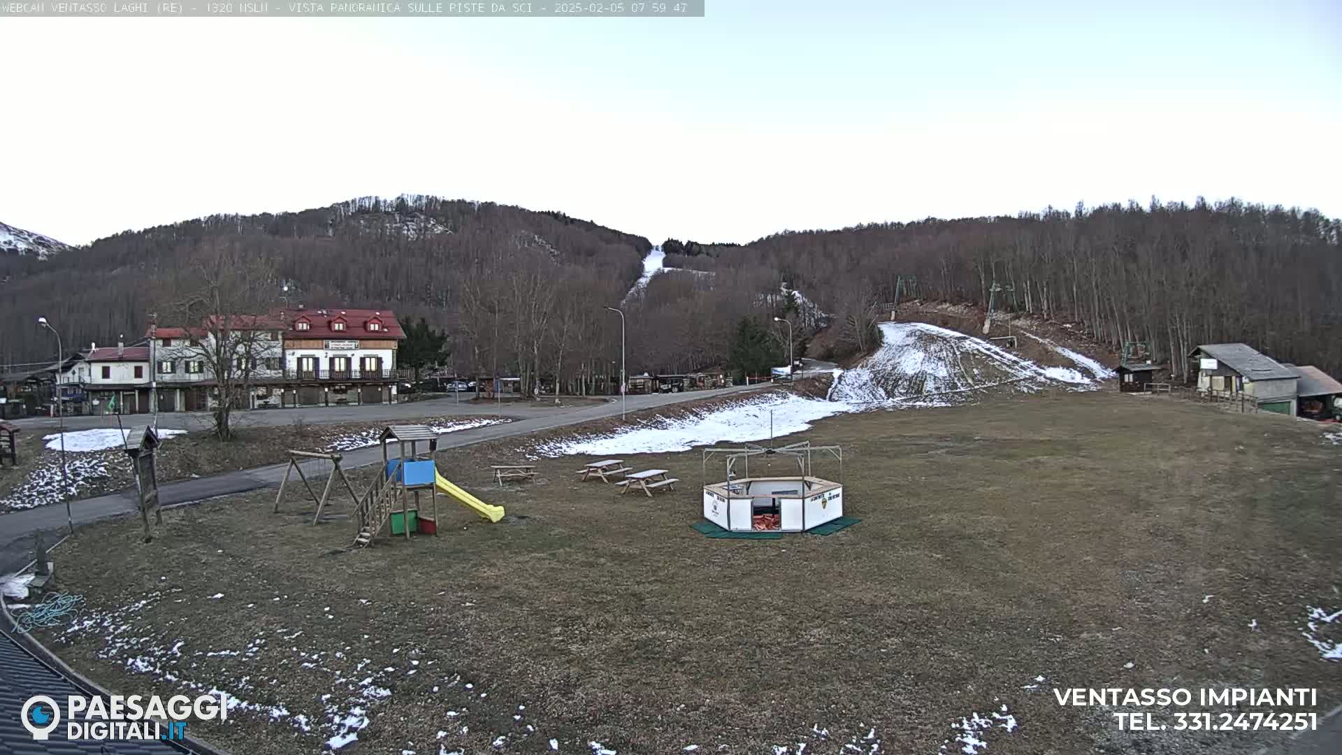 A playground and picnic tables sit in a grassy area near a ski slope and buildings, under a mostly clear sky.