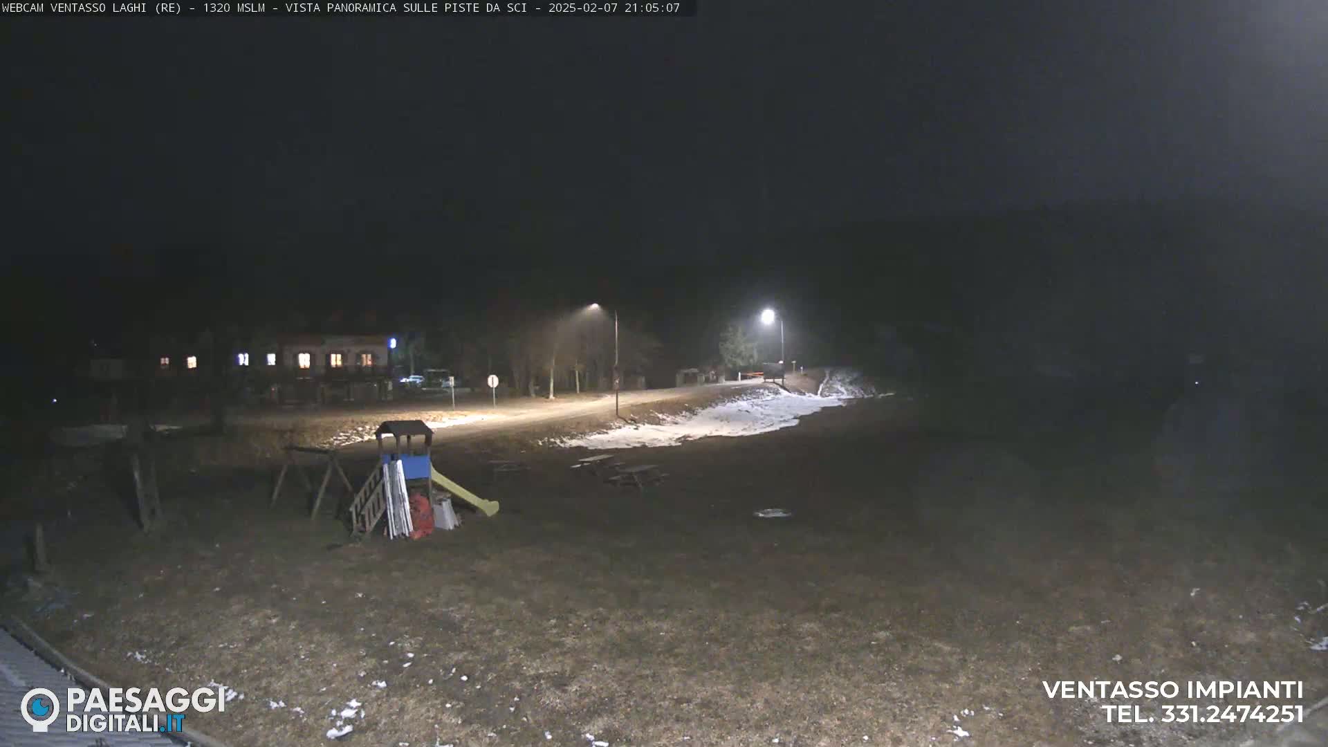 A nighttime view of a playground and a road with some snow on the ground, illuminated by streetlights.