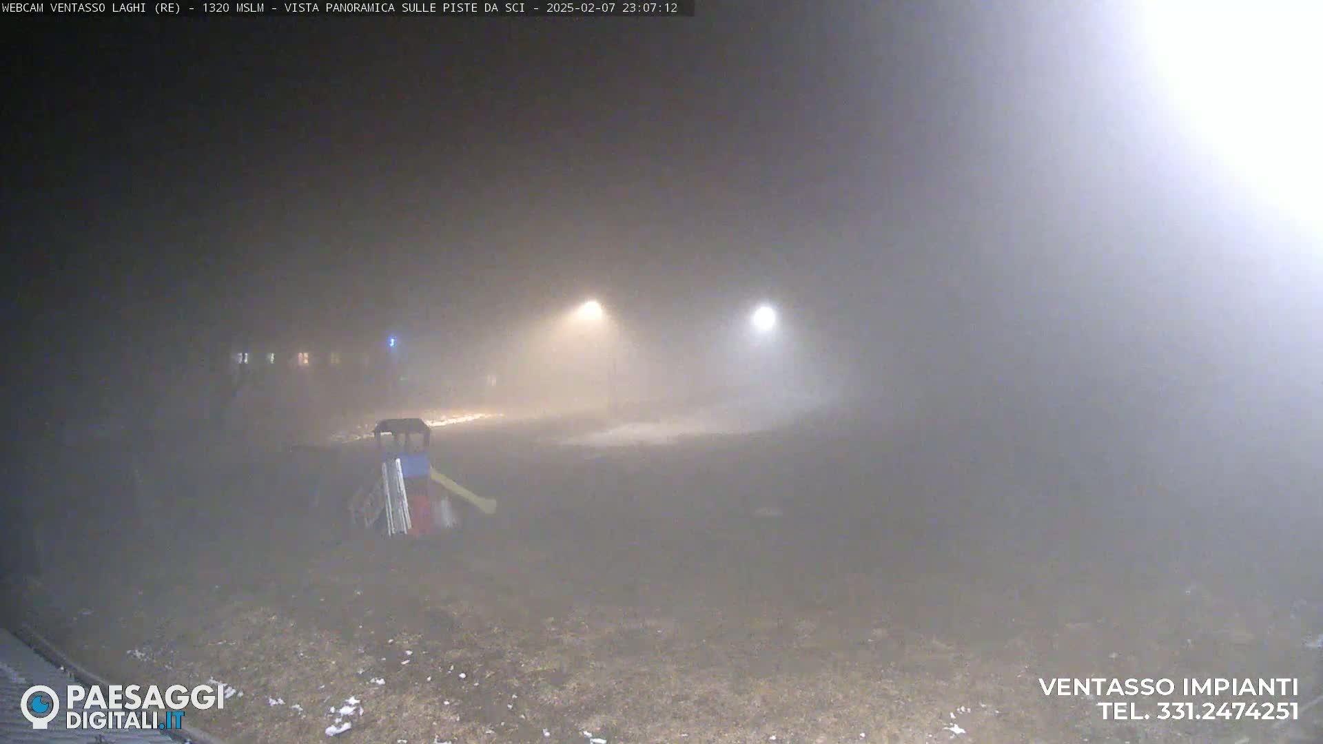 A foggy, nighttime scene shows a playground with a slide and some other structures, dimly lit by two distant streetlights.