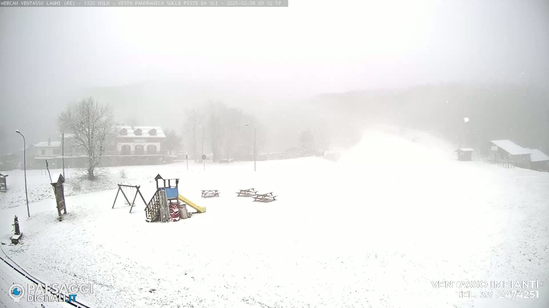 A snow-covered playground with picnic tables is visible in the foreground, while a building and trees are faintly seen in the background under heavy snowfall.