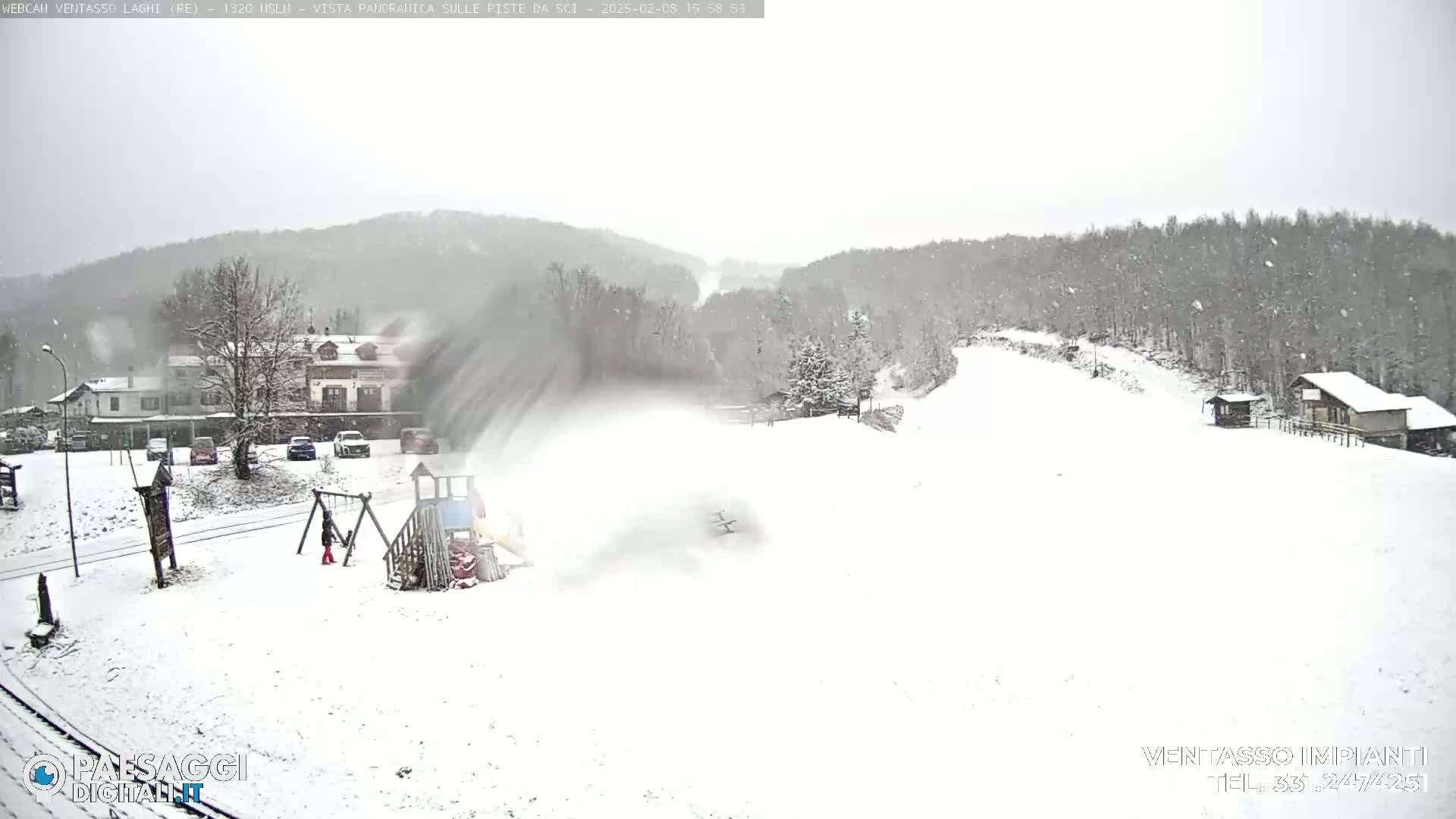 A snow-covered playground and ski slope are visible, with snow falling heavily in the background of a wooded hillside.