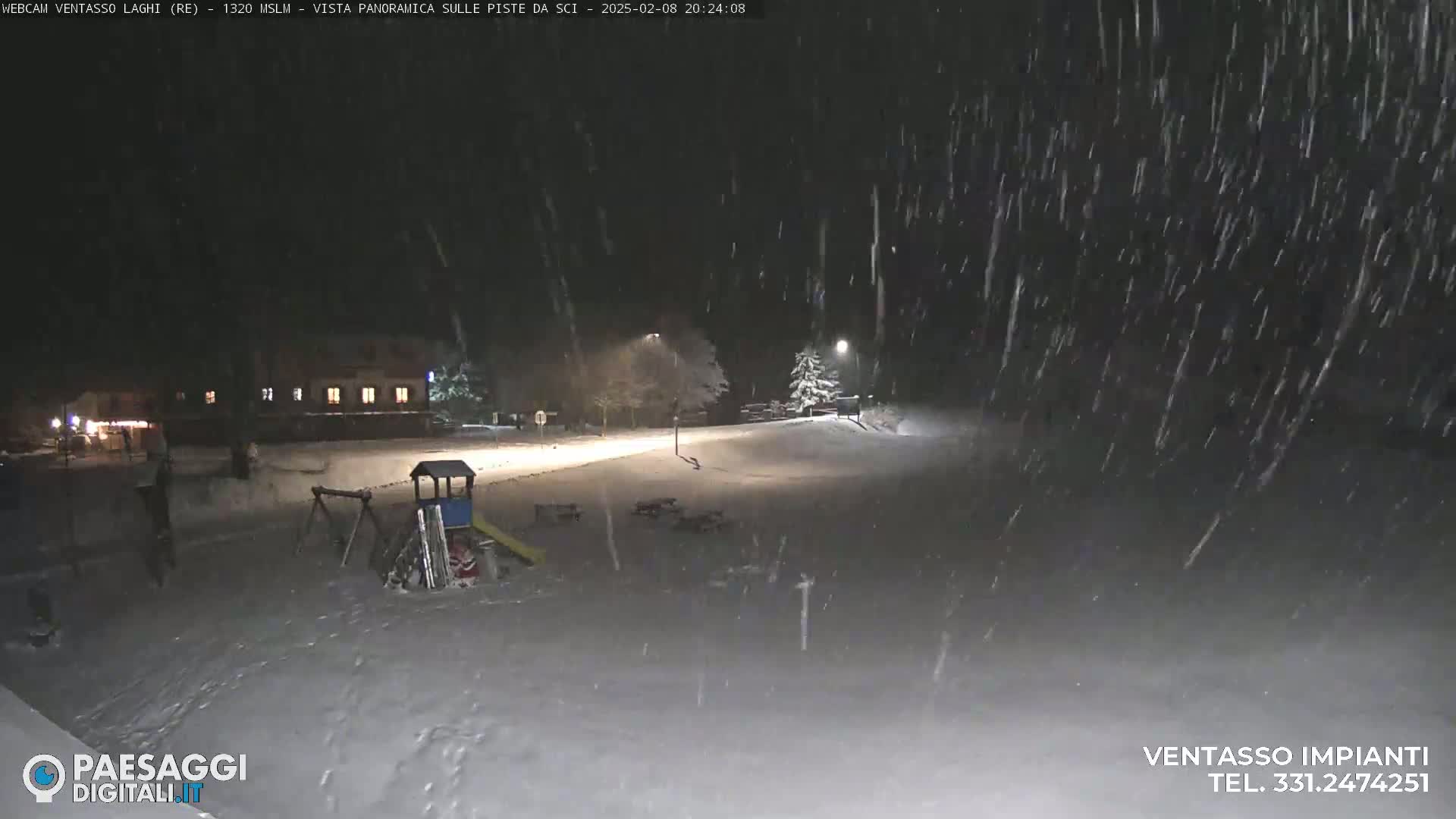 A snow-covered playground and a building are visible at night under heavy snowfall.