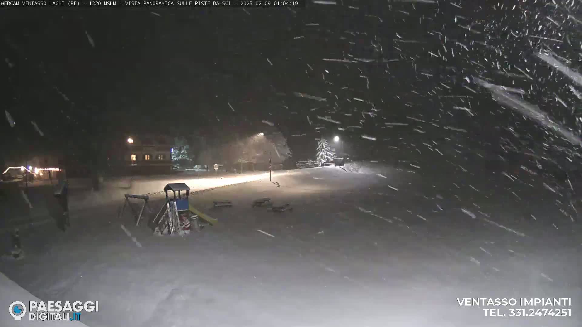 A snow-covered playground and a building are visible under heavy snowfall at night, illuminated by streetlights.