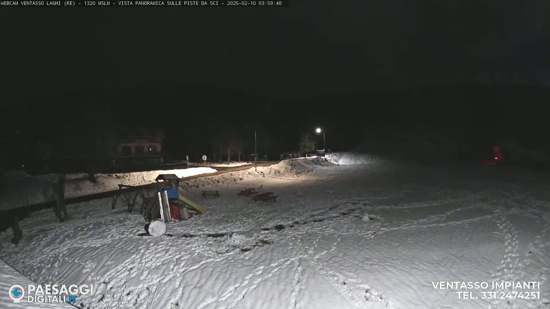 A snow-covered playground area is illuminated at night by artificial light.