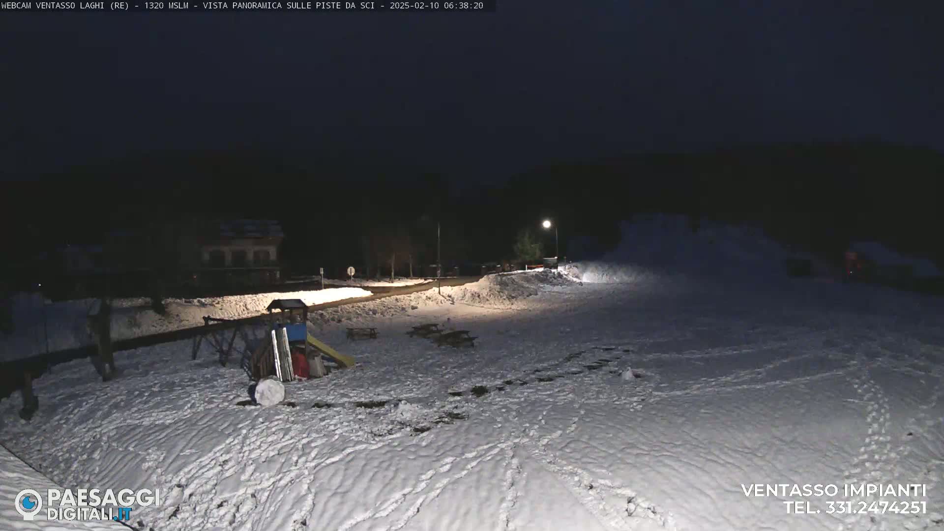 A snow-covered playground and parking area are visible at night, illuminated by a single streetlight.