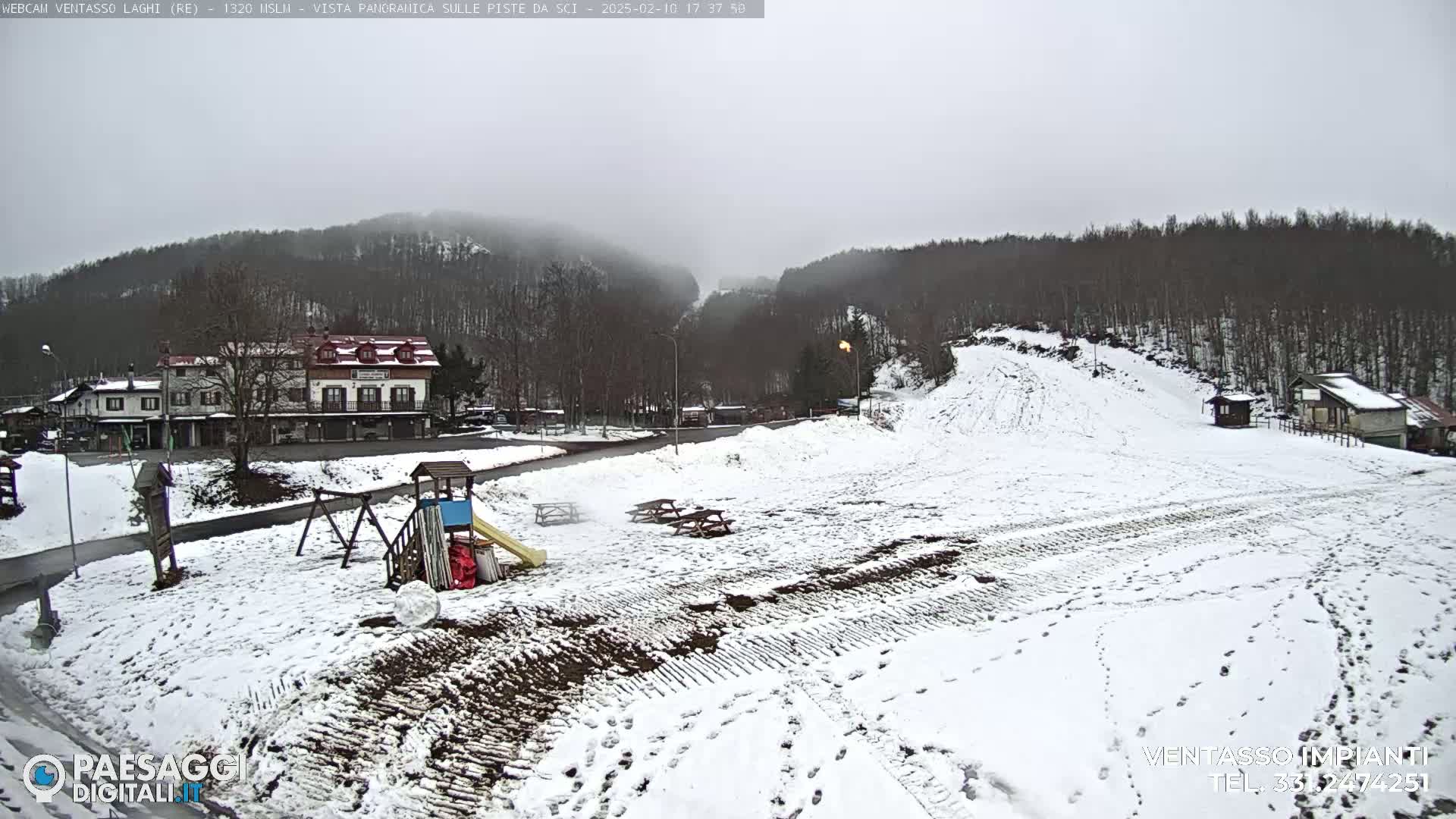 A snow-covered ski slope with a building, playground, and picnic tables is visible under an overcast sky.