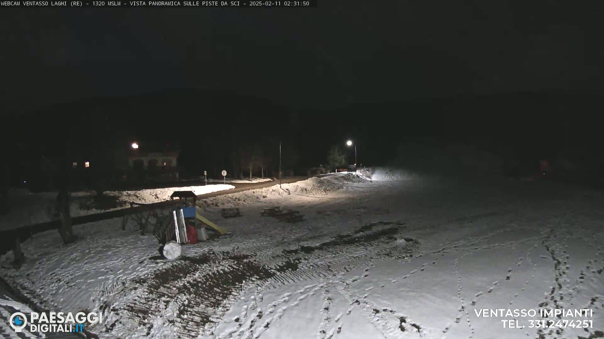 A snow-covered area at night, illuminated by artificial lights, with a playground visible in the background.