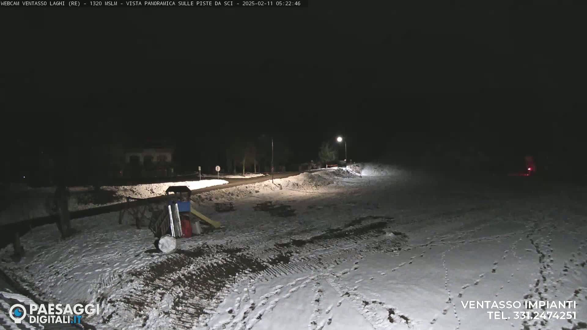 A snow-covered area at night, illuminated by artificial lights, with some equipment and footprints visible.