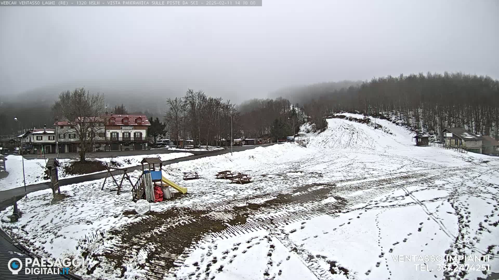 A snow-covered playground and ski slope are visible in a foggy, wintry landscape, with buildings in the background.