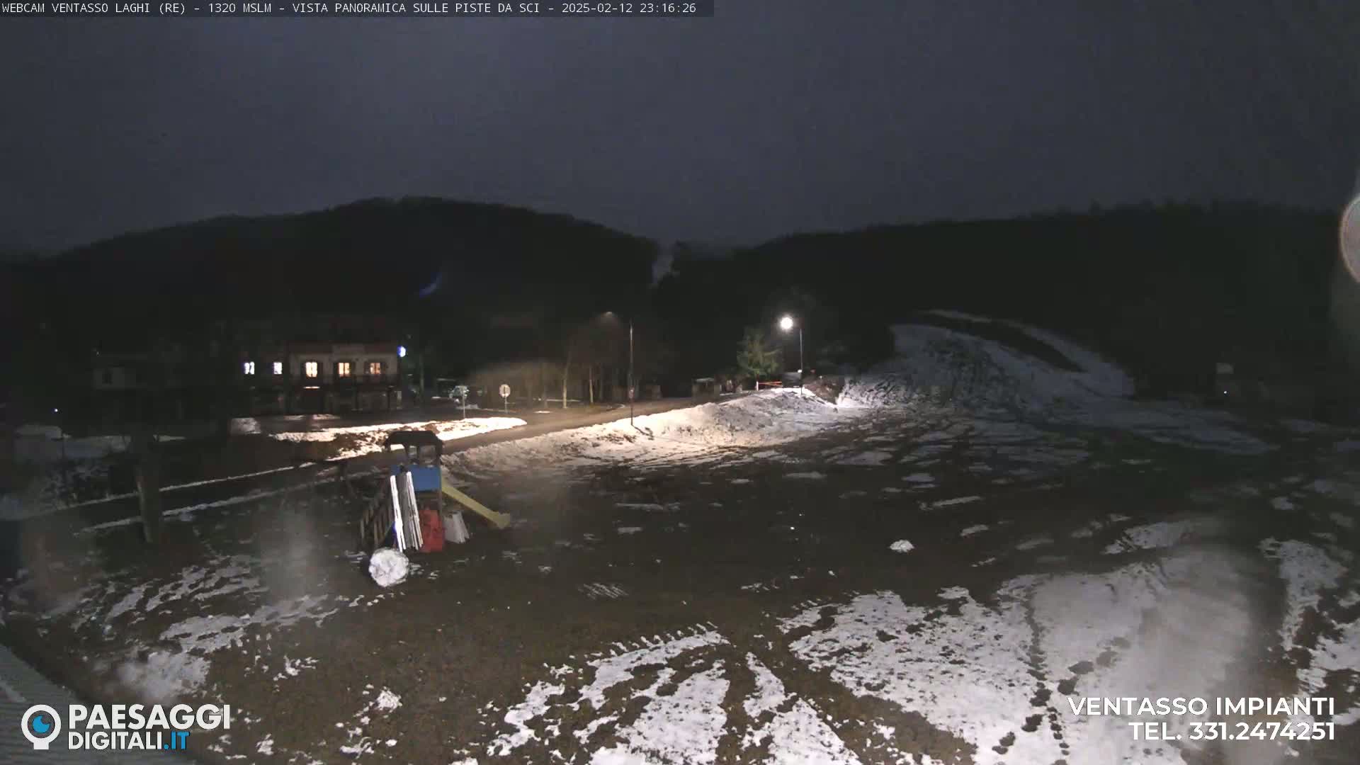 A nighttime view of a snow-dusted, sparsely populated area with a building and playground equipment, under a dark, overcast sky.