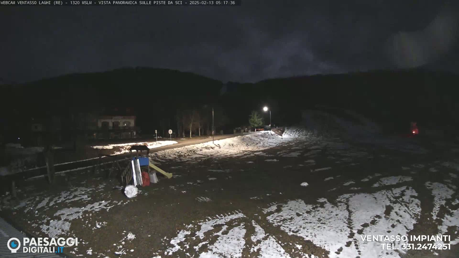 A nighttime, snow-dusted ground scene with a few buildings and playground equipment visible under a dark, cloudy sky.