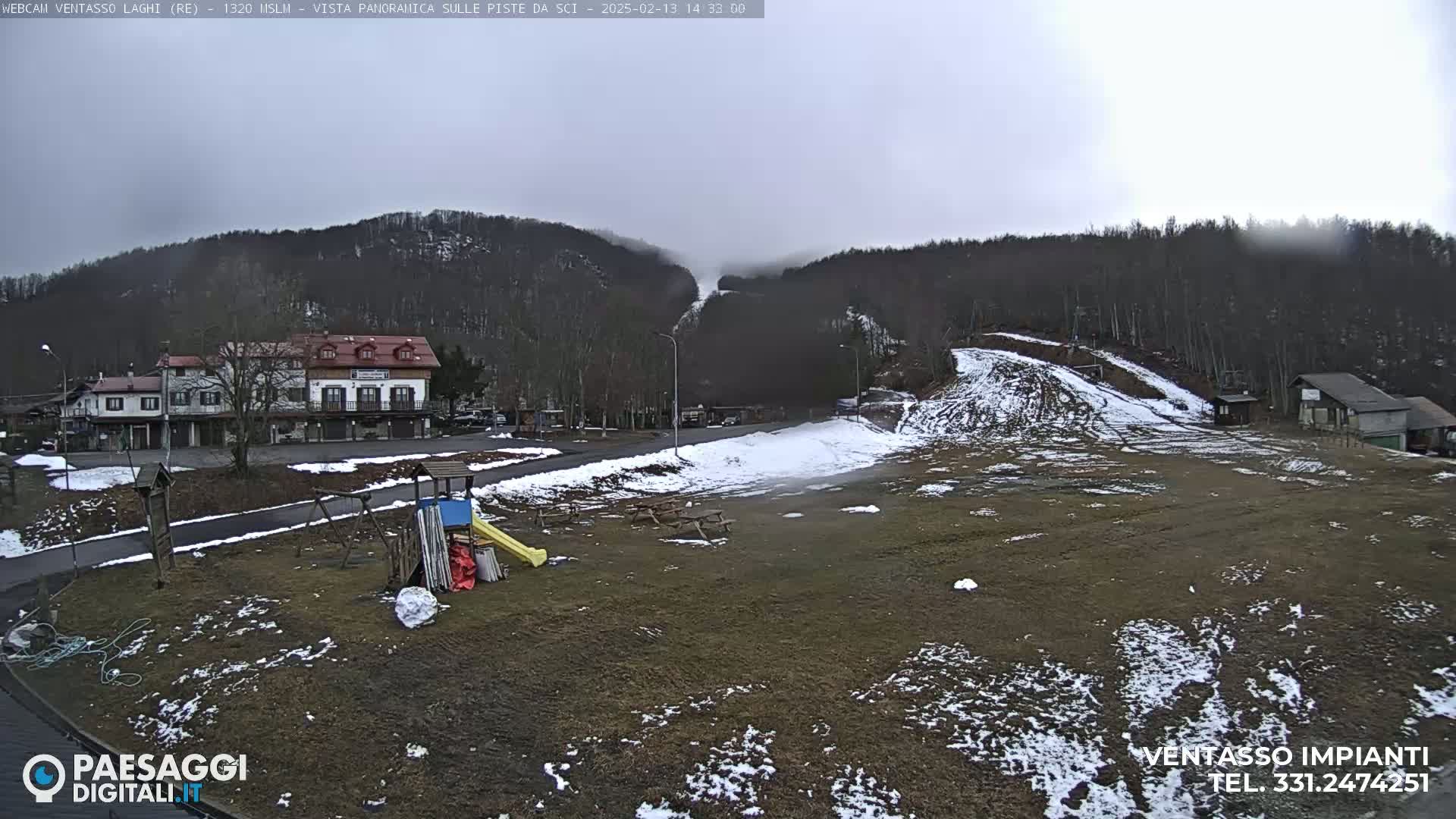 A mostly cloudy day reveals a snow-dusted playground and ski slope nestled in a valley between leafless hills.