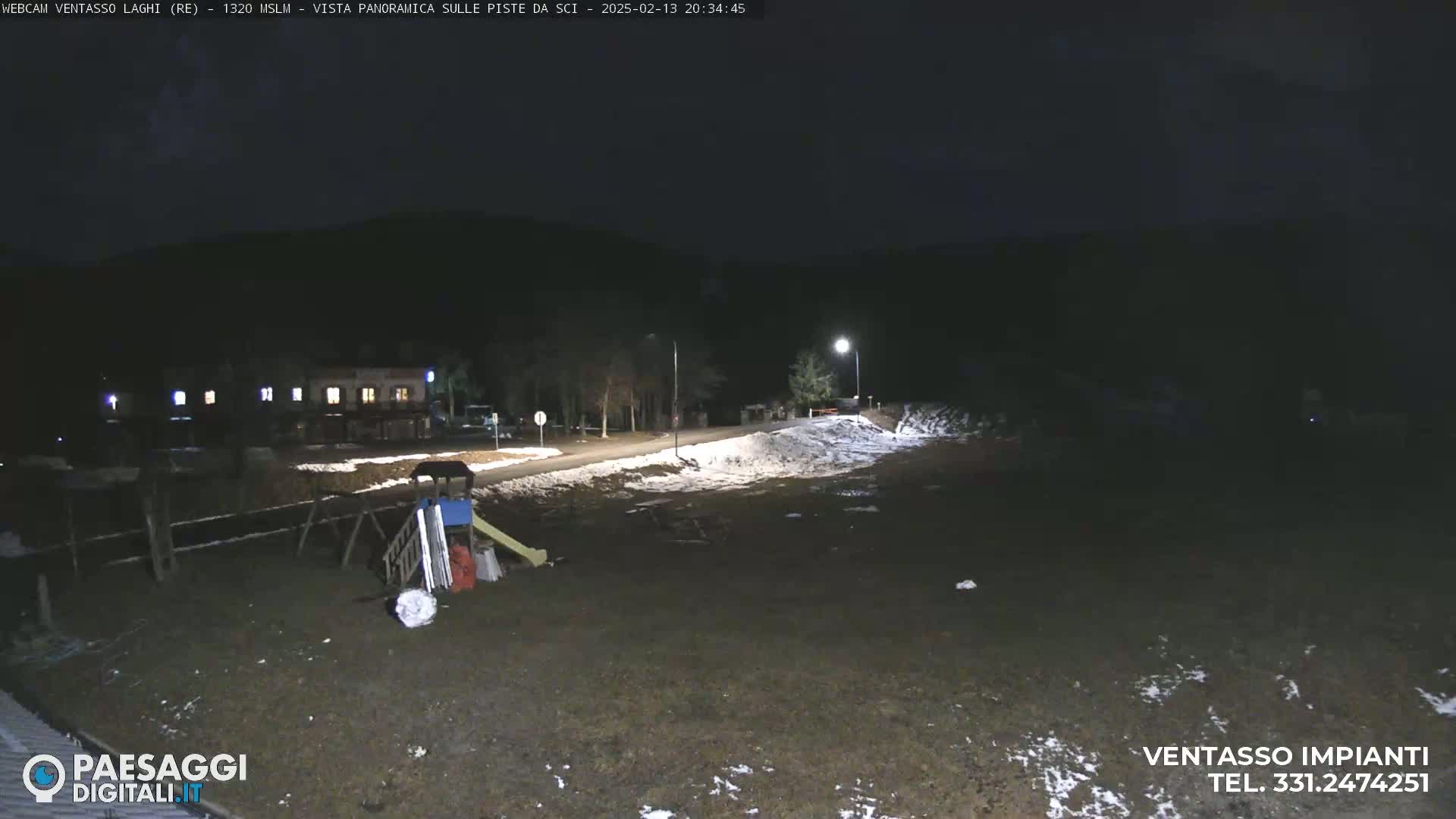 A nighttime scene shows a playground with some snow on the ground near a building under a dark sky.