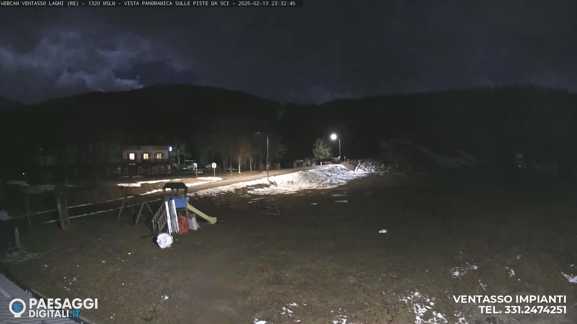 A nighttime scene of a playground and a road with patches of snow, under a partly cloudy sky.