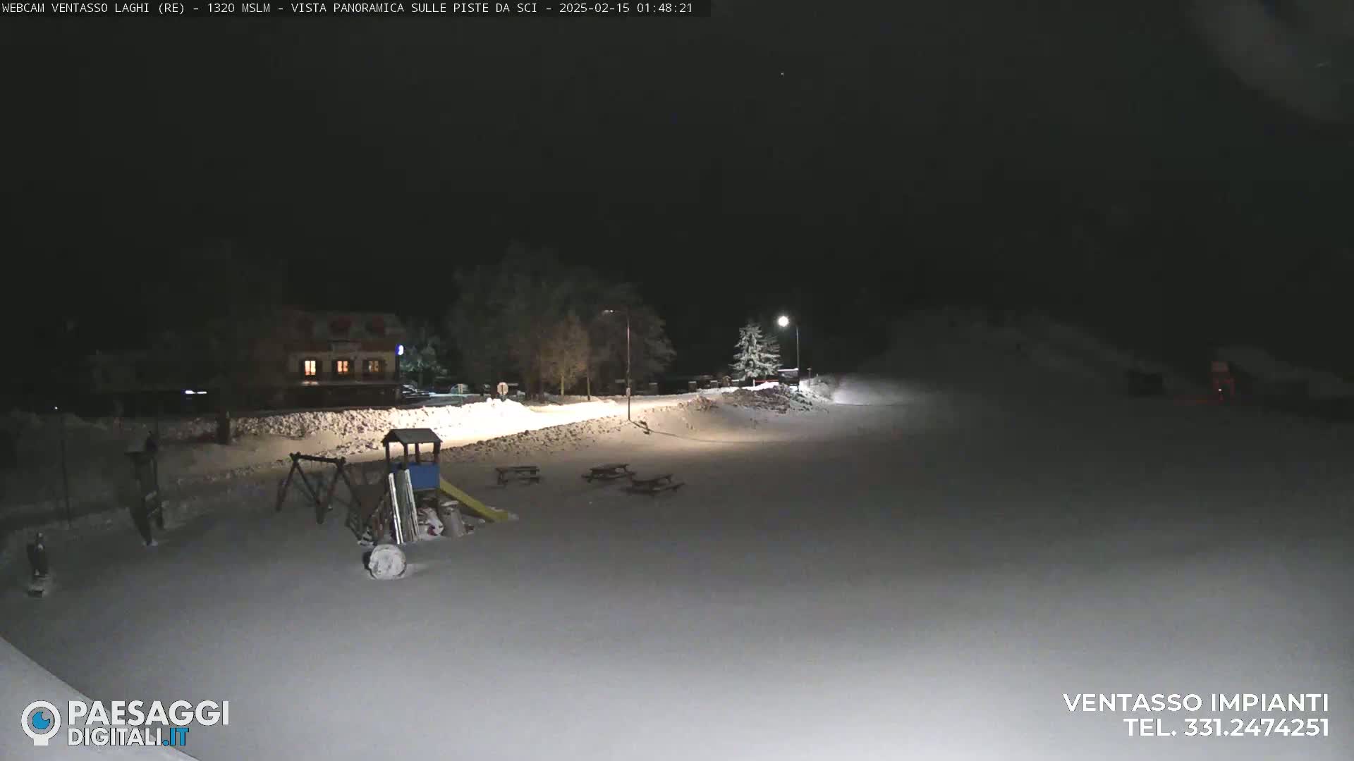 A snow-covered playground and picnic area are visible at night under a dark, clear sky, illuminated by streetlights.