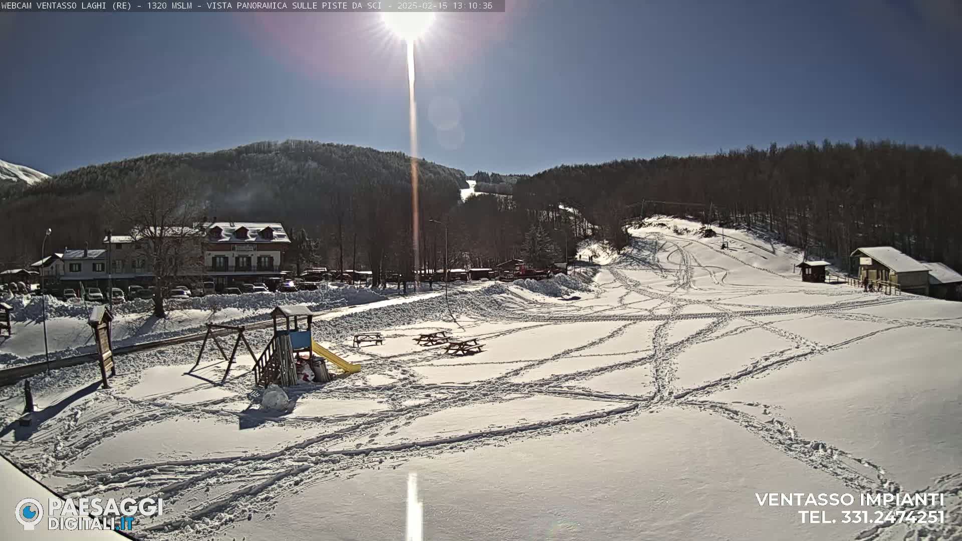 A snow-covered ski resort on a sunny day, showing ski runs, a building, a playground, and picnic tables.
