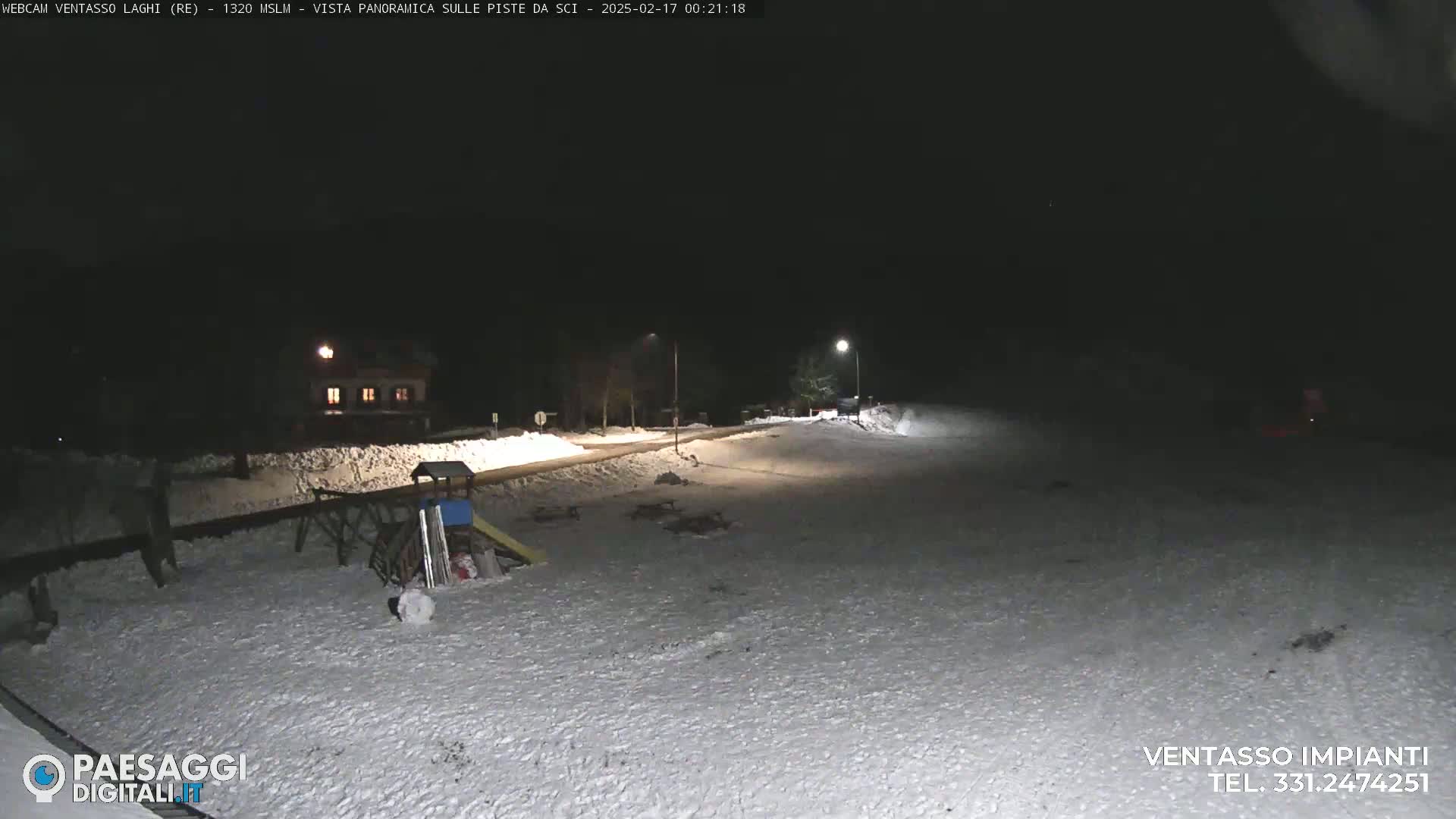 A snow-covered playground and road are illuminated at night by streetlights.