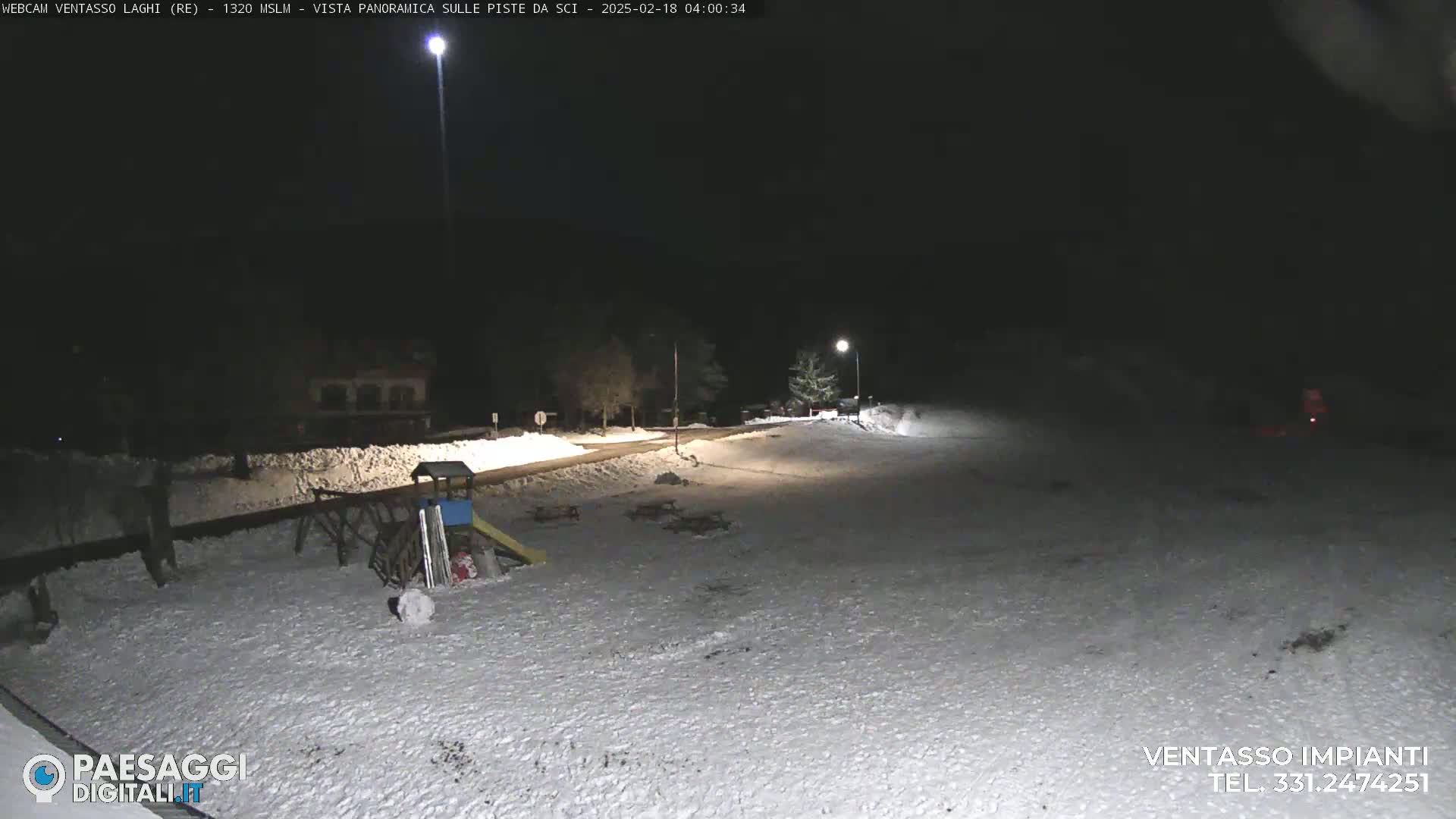 A snow-covered playground and road are illuminated at night by streetlights.