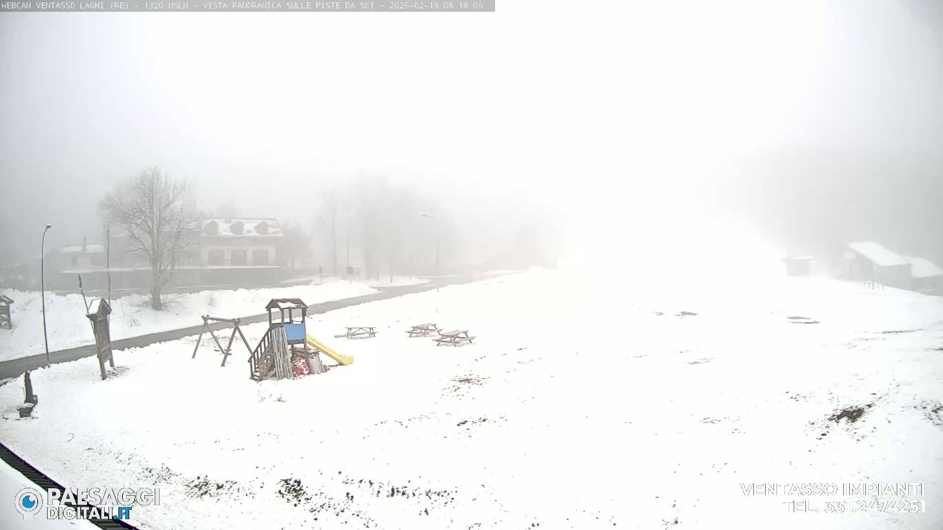 A snow-covered playground with picnic tables is visible in the foggy distance, with buildings barely discernible through the heavy fog.