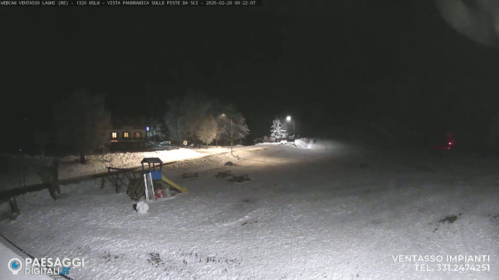 A snow-covered playground and surrounding area are illuminated at night by streetlights.