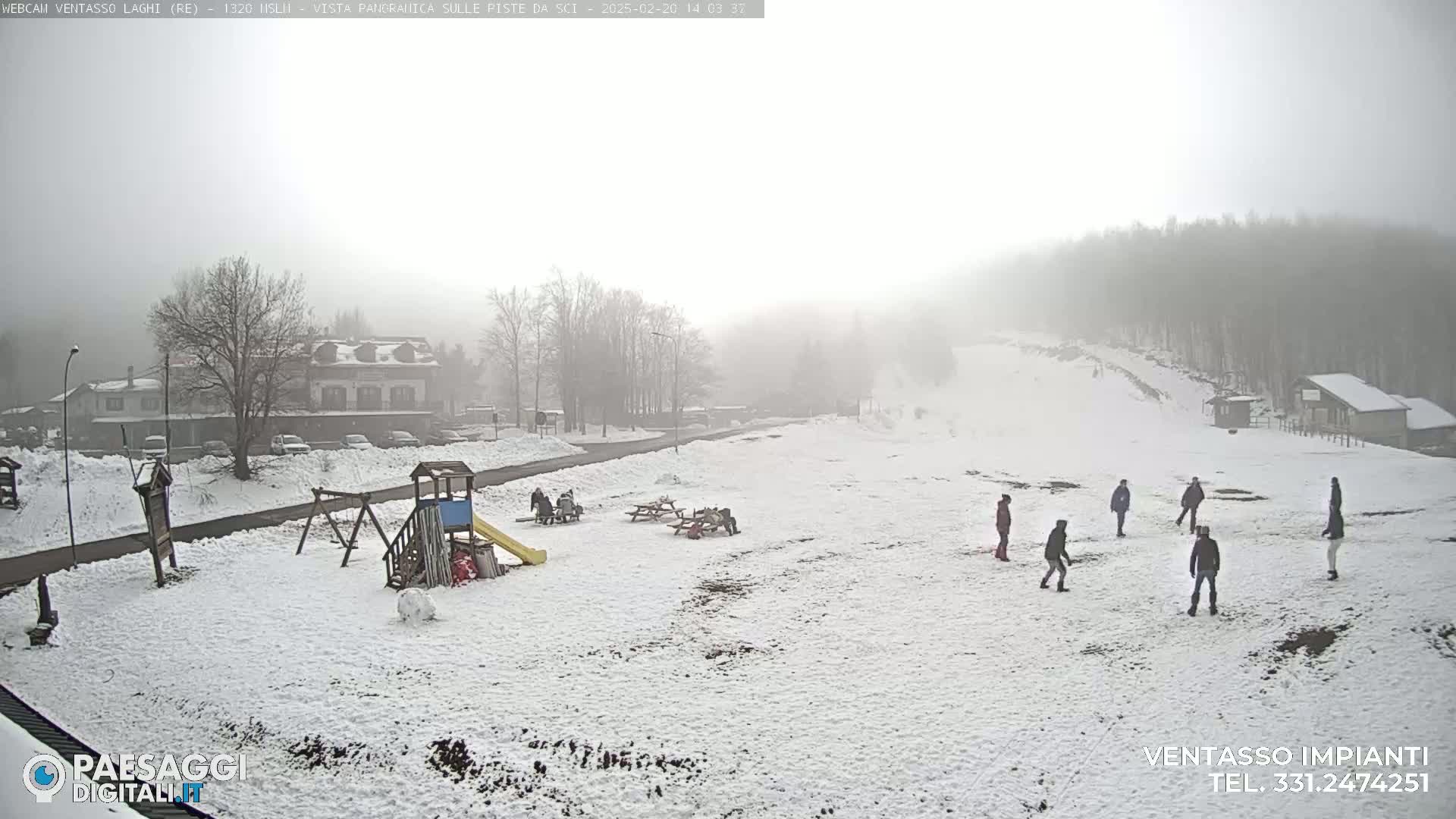 A snow-covered playground and surrounding area are visible in a foggy, snowy landscape with several people playing in the snow.