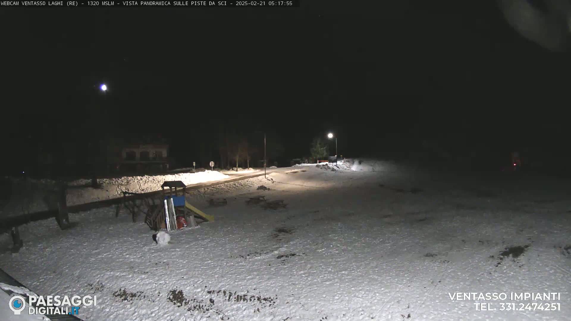 A snow-covered playground and roadway are illuminated at night under a clear sky.
