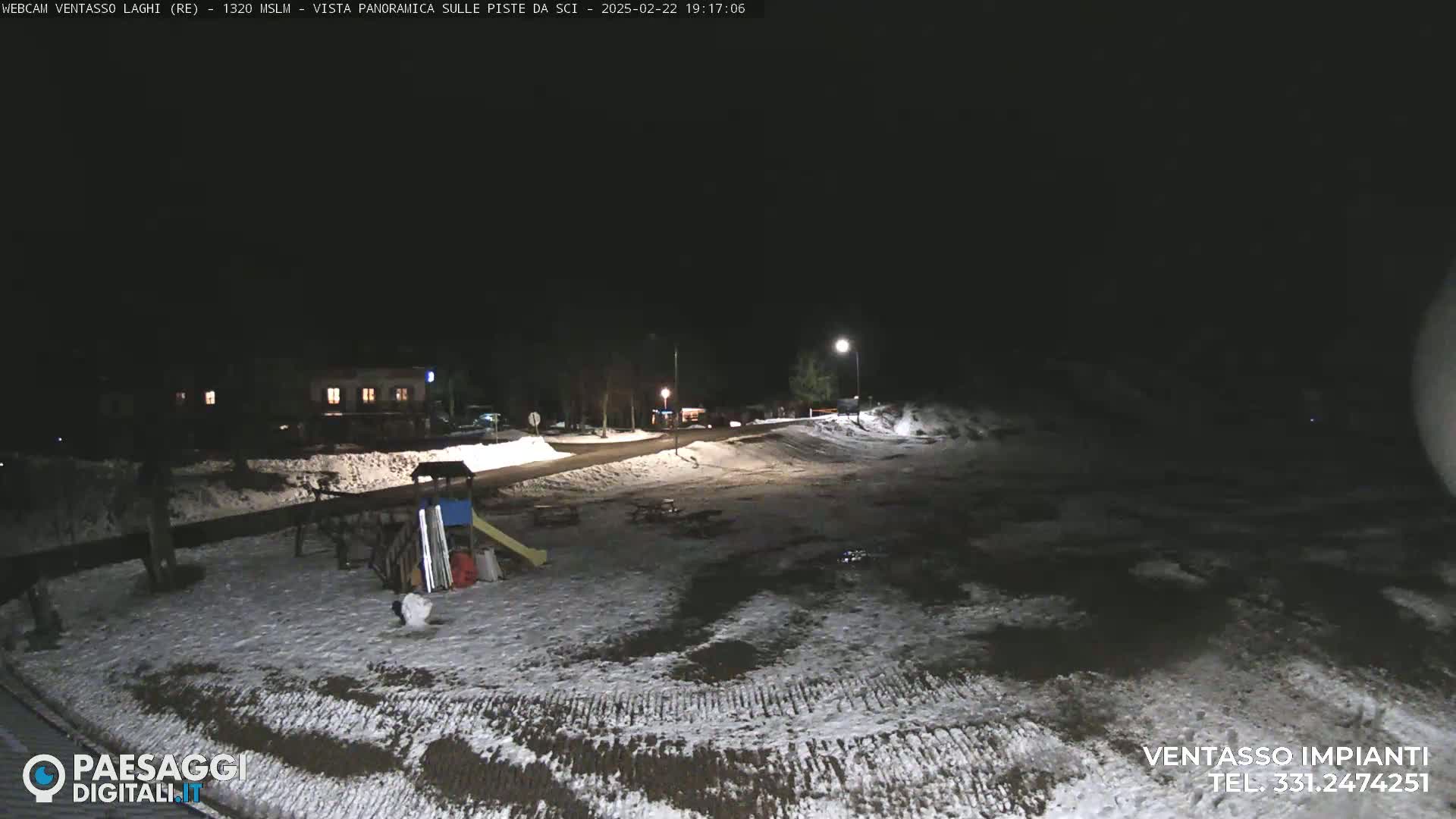 A snow-covered, nighttime scene shows a sparsely populated area with a building, playground equipment, and a road.