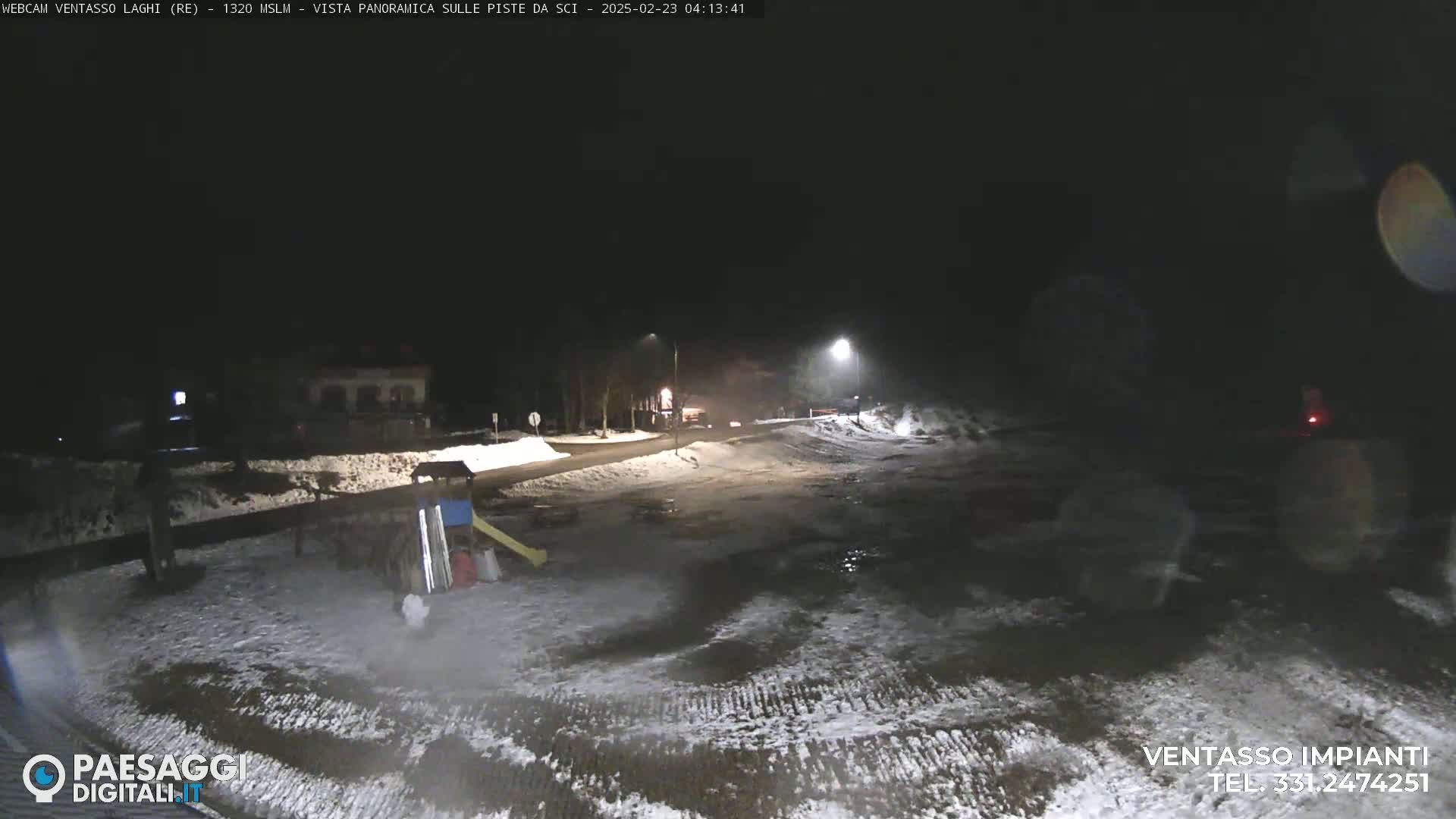 A nighttime view of a snow-covered road and playground, illuminated by streetlights.