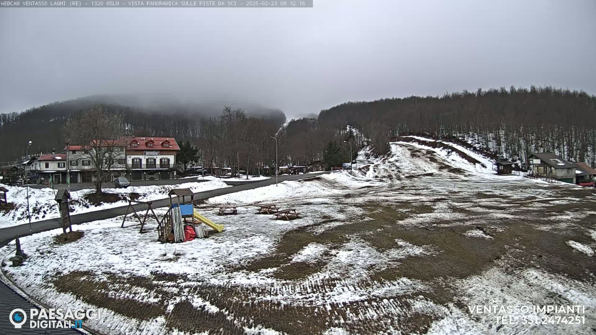 A snowy, overcast scene shows a small town nestled in a hilly, wooded area with a playground and ski slope visible.