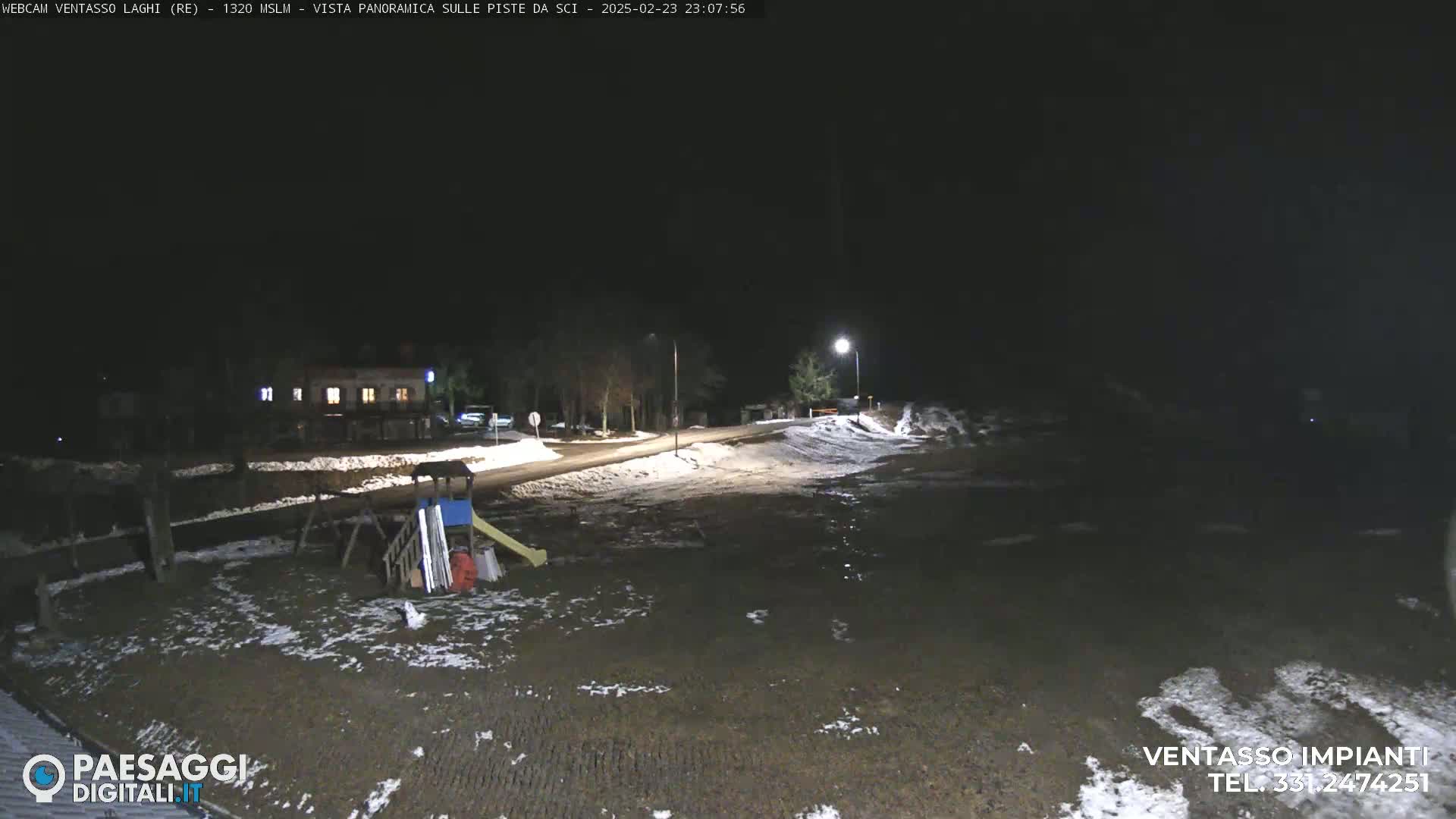 A nighttime, snow-dusted scene shows a road, a building, and a playground area illuminated by streetlights.