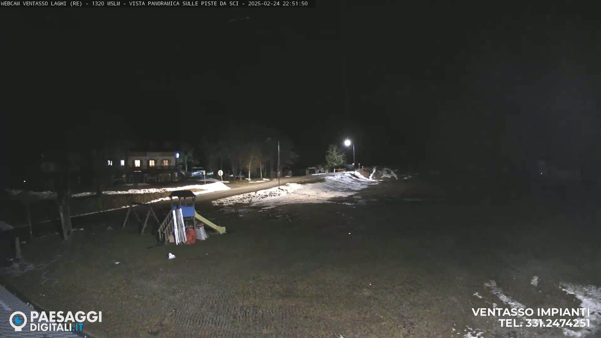 A nighttime view of a playground near a road with some snow on the ground under a dark sky.