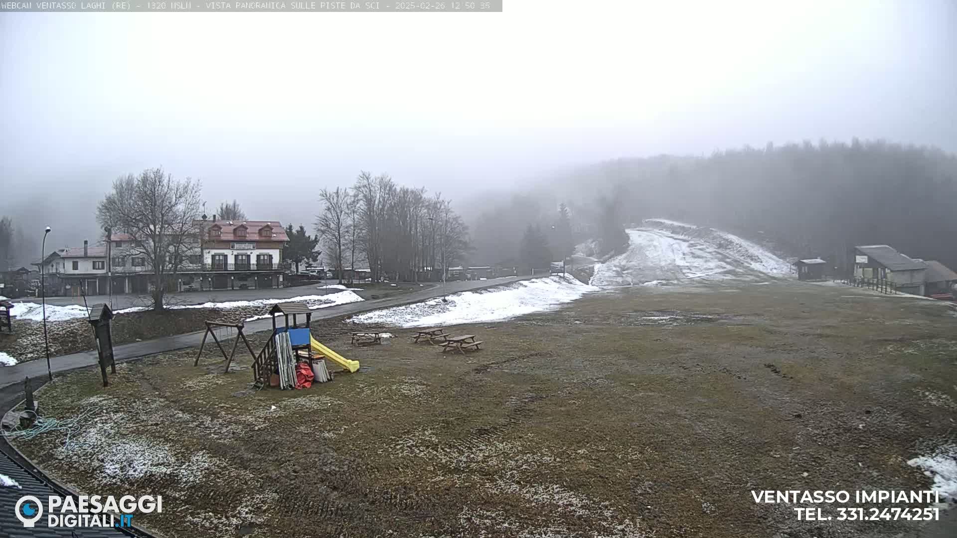 A foggy view of a snow-dusted ski slope, a playground, and buildings, with some patches of snow on the ground.