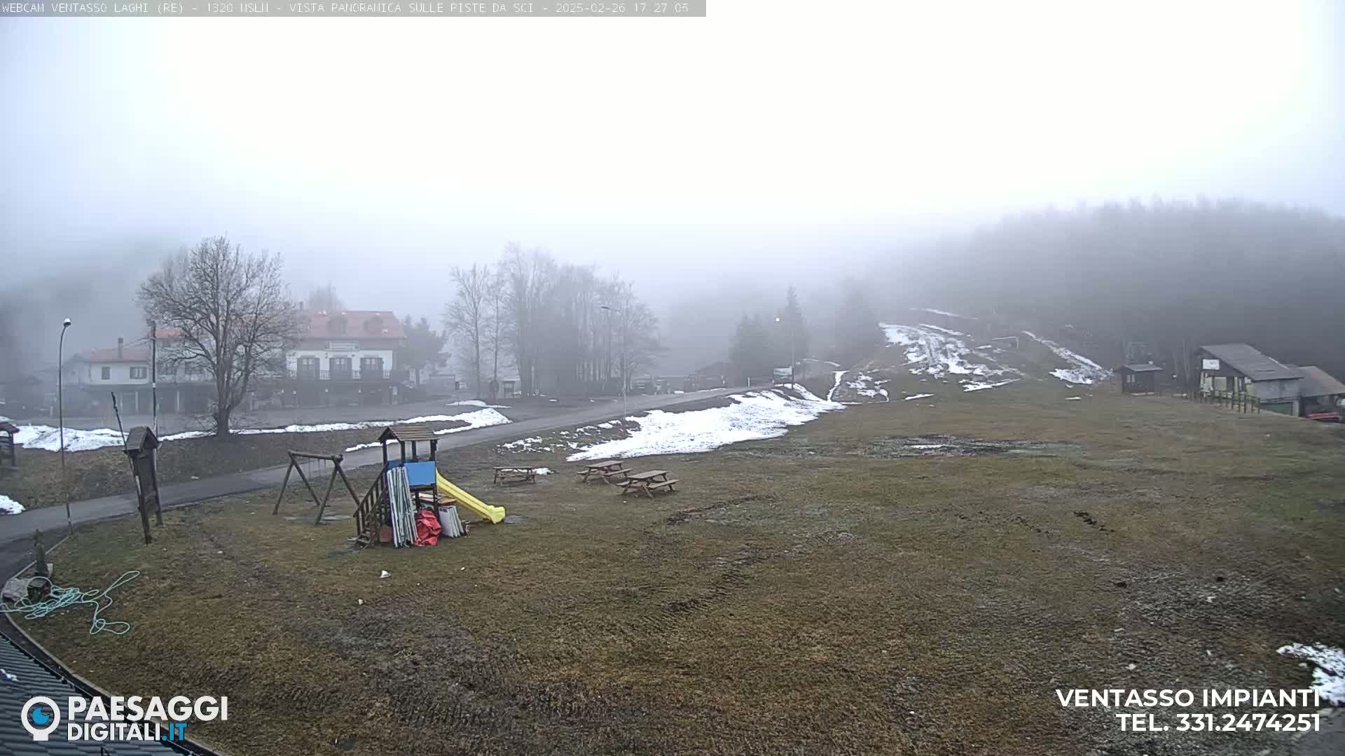 A foggy, snow-dusted landscape shows a playground, picnic tables, and buildings in the distance.