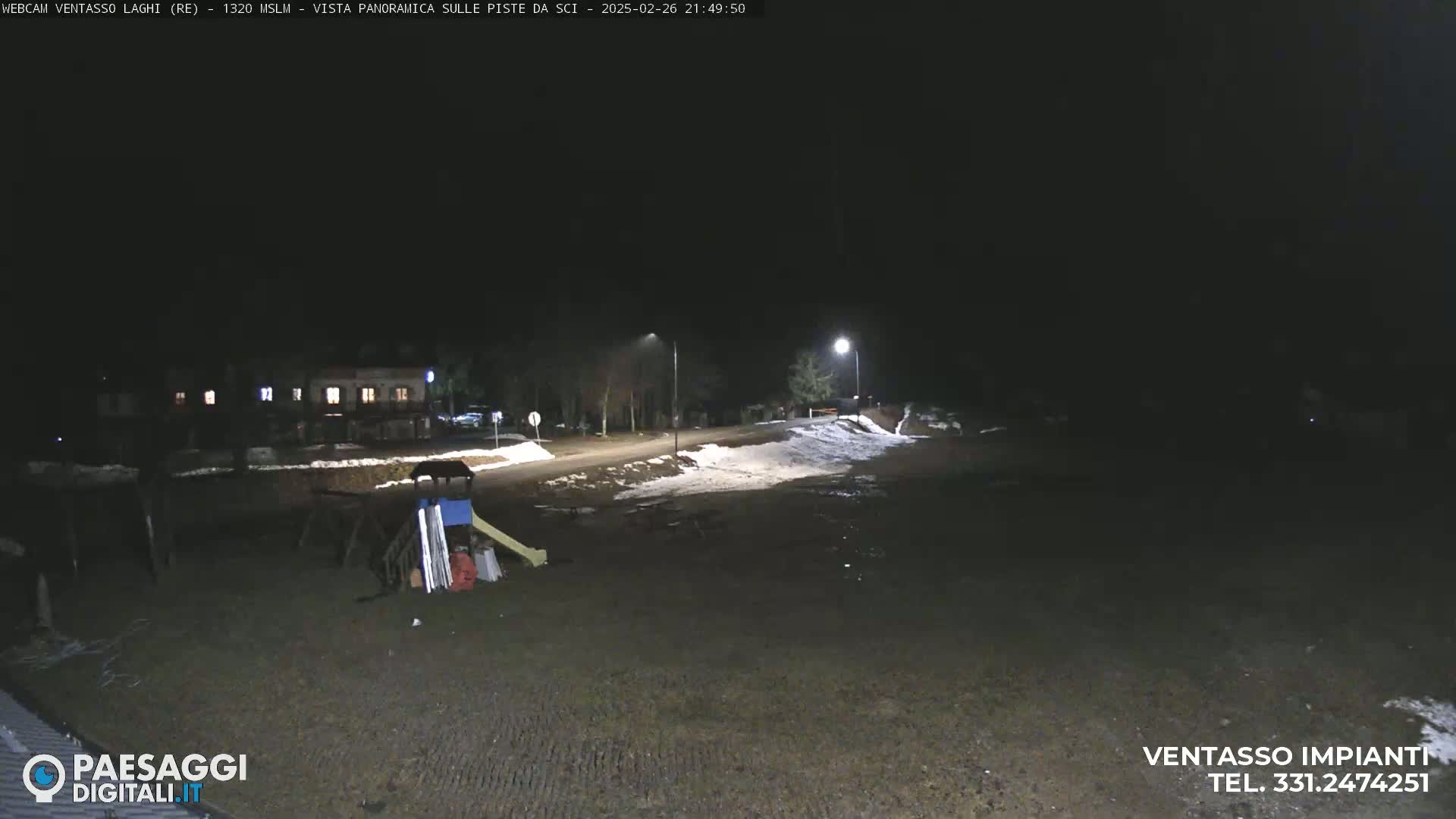 A nighttime view of a snow-covered area near a road and a building, with a playground visible in the foreground.