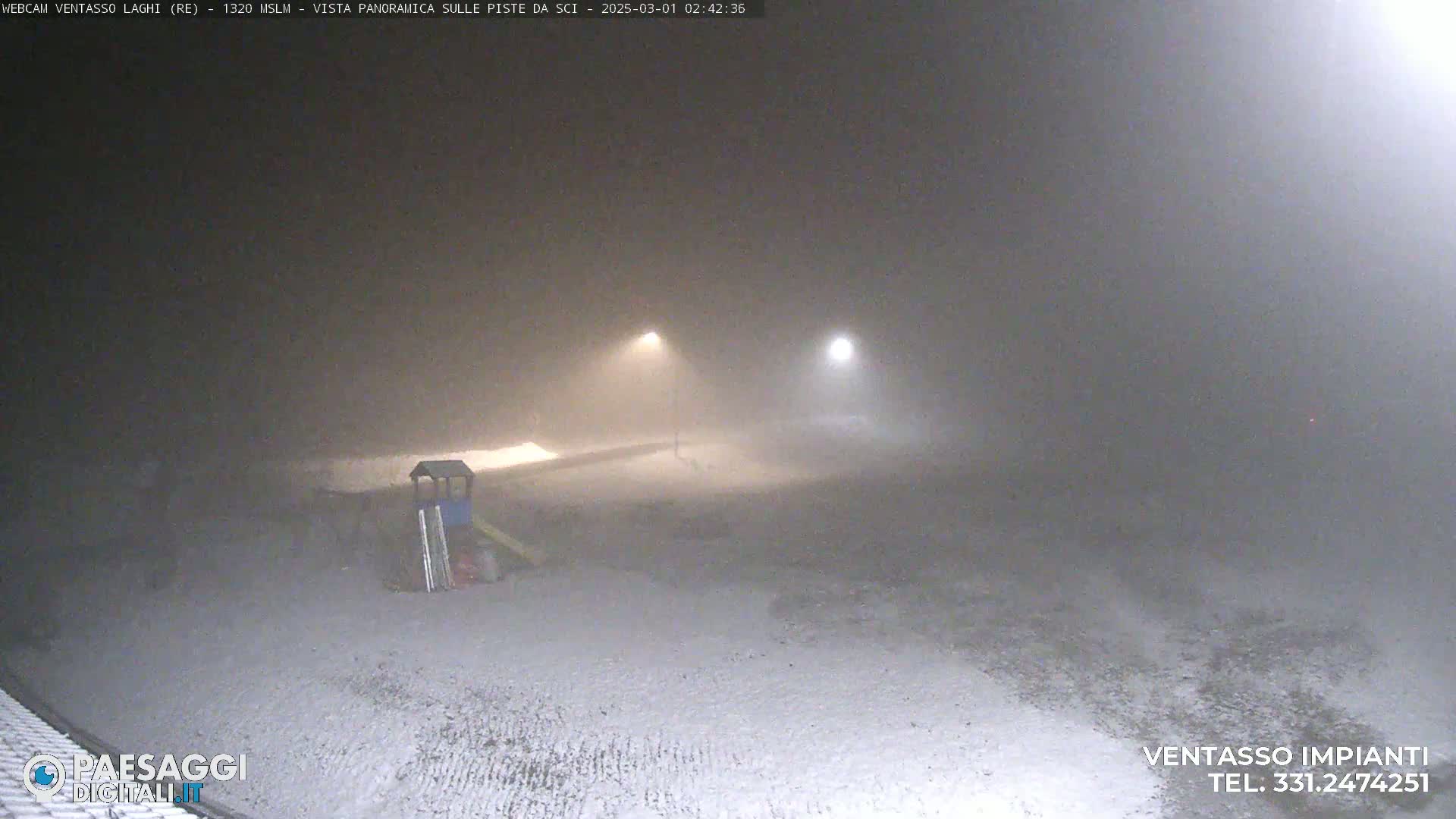 A snow-covered area at night is dimly lit by two lights in heavy fog or snow.