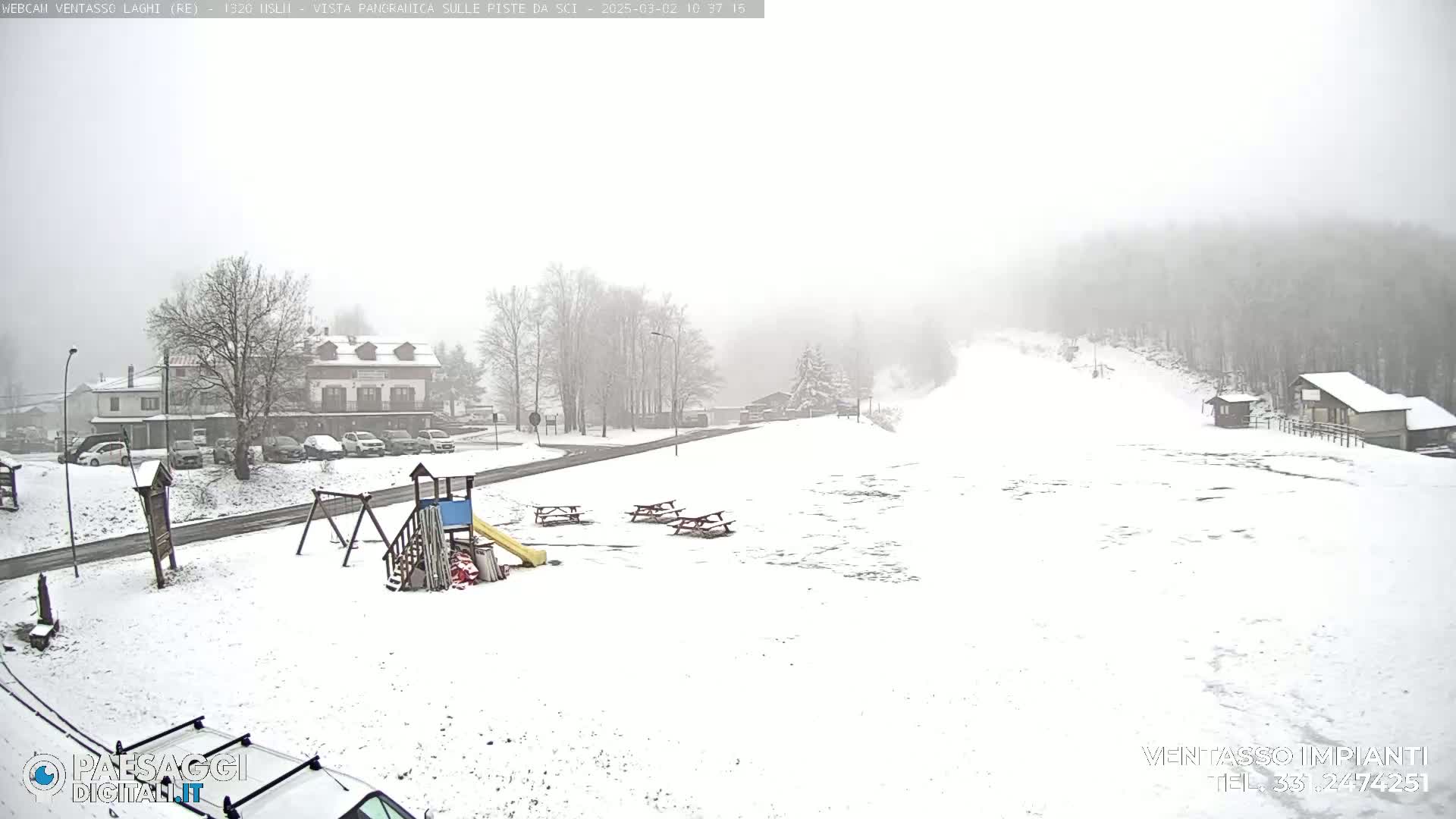 A snow-covered playground and parking lot are visible, with snow falling heavily in a mountainous, foggy landscape.