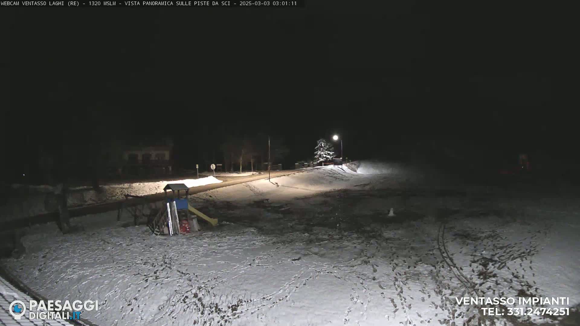 A snow-covered playground and road are illuminated at night under dark skies.