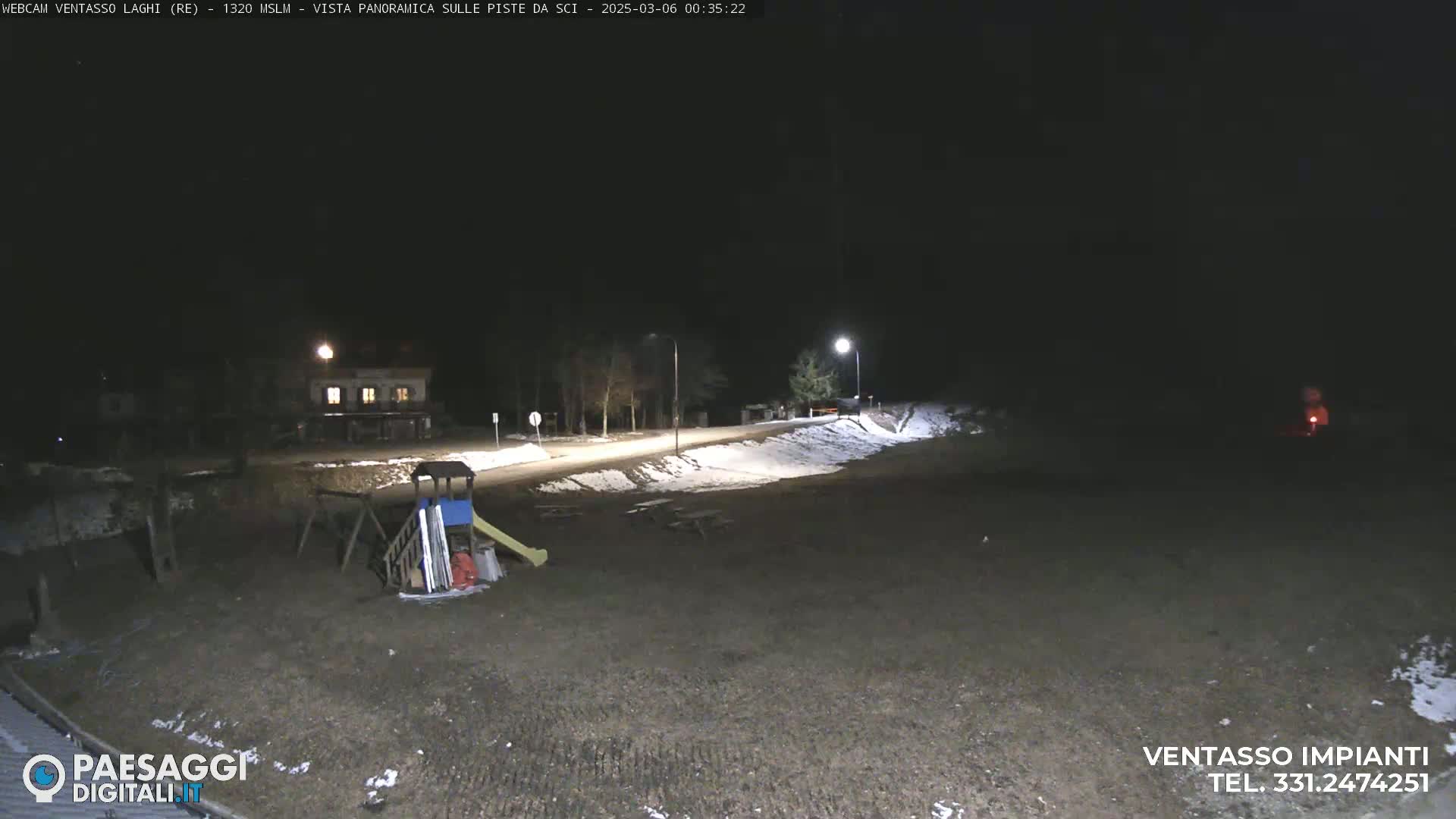 A nighttime, snow-dusted scene shows a playground, picnic tables, and a building, lit by streetlights.