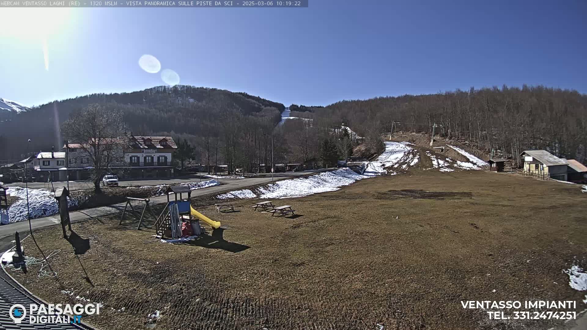 A sunny day reveals a ski resort with a playground, picnic tables, and a partially snow-covered ski slope in the background.