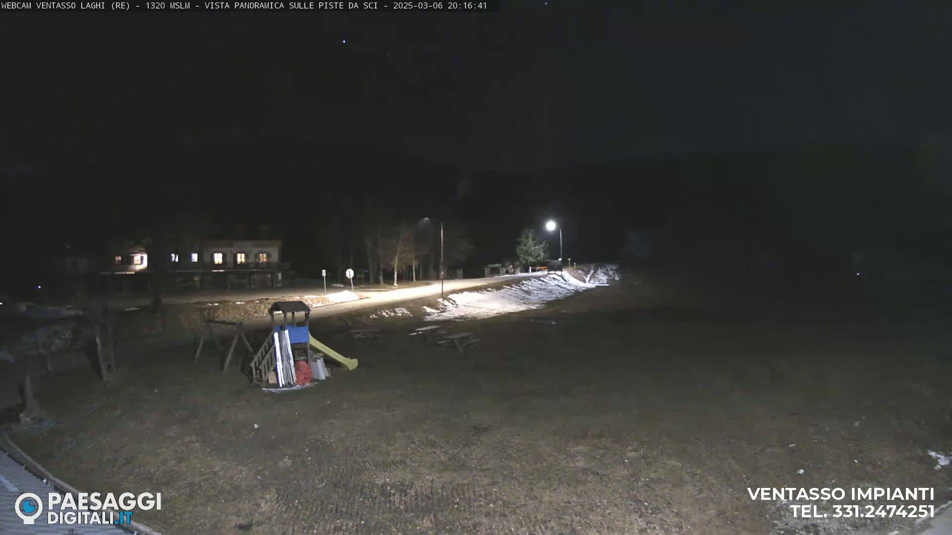 A nighttime view of a playground and a road with some snow on the ground, under a dark, clear sky.
