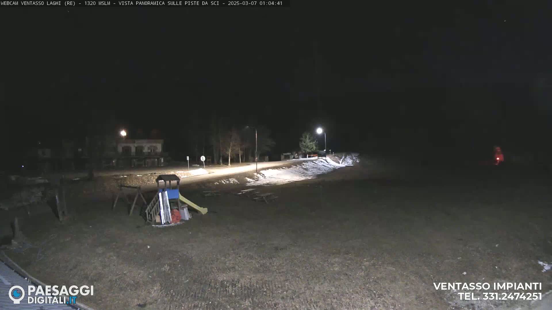 A nighttime view of a playground and a road with some snow on the ground, lit by streetlights.