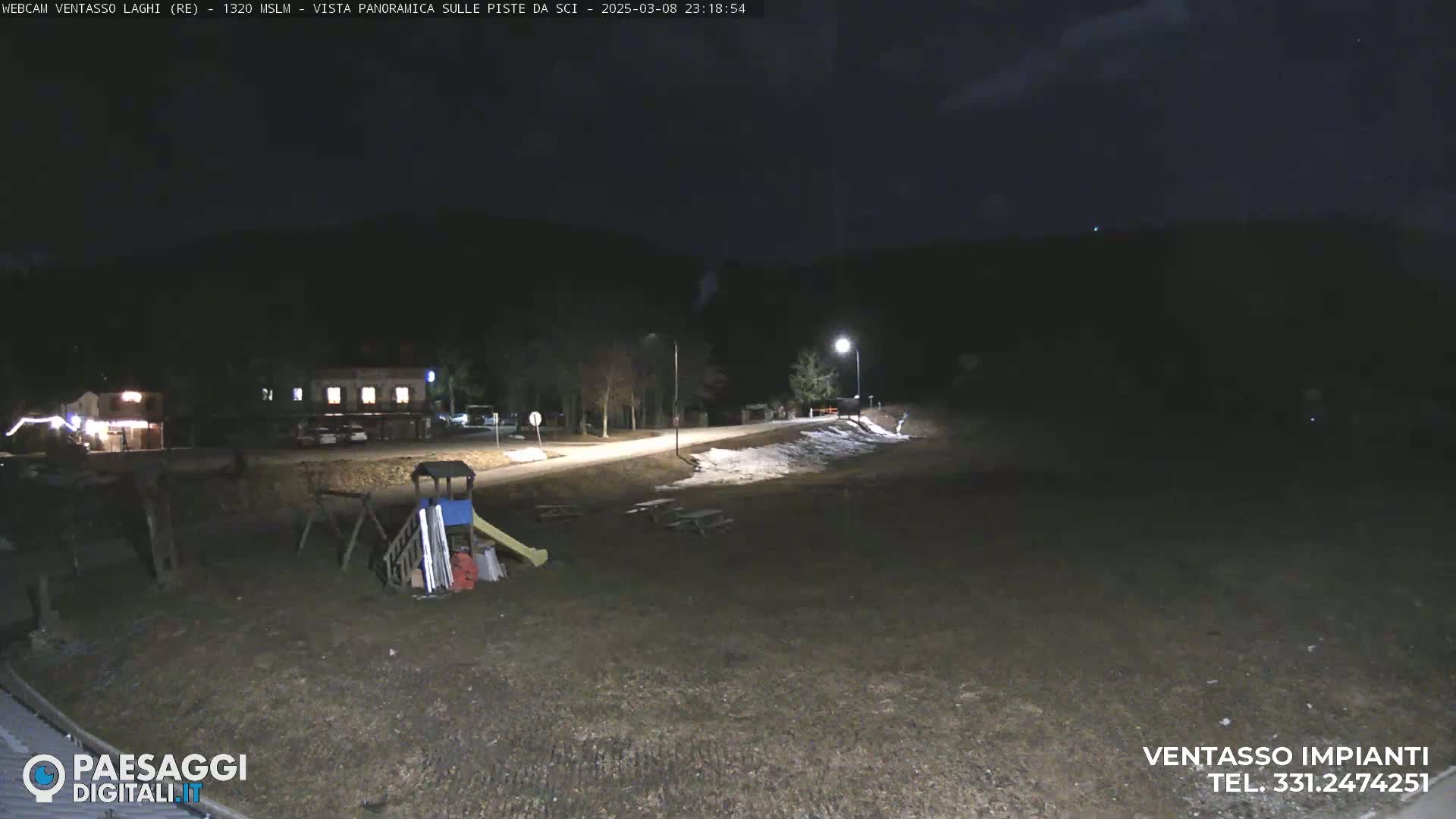 A nighttime outdoor scene shows a paved road, a building in the distance, a playground, and patches of snow on the ground under partly cloudy skies.