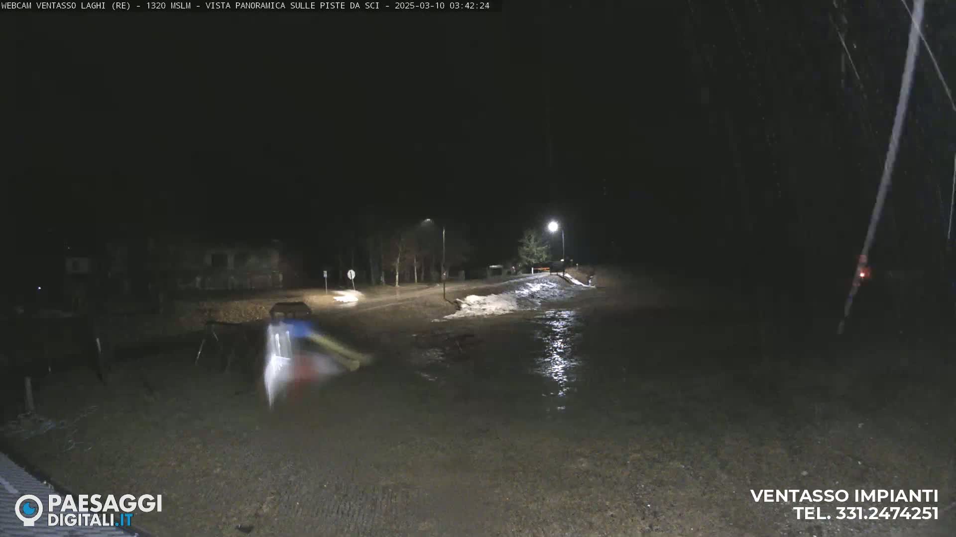 A nighttime scene shows a flooded road under dim streetlights, with some snow visible nearby.