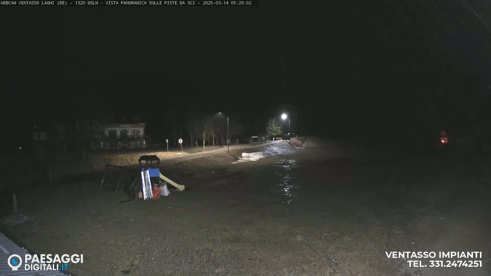 A nighttime view of a mostly dark, flood-lit area shows a partially flooded road, a playground with some equipment, and a building in the distance.