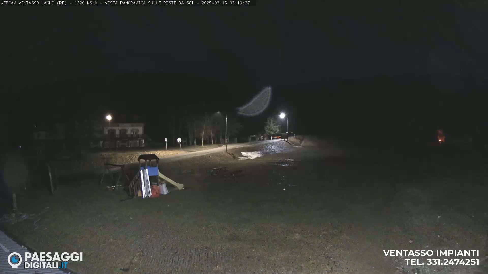 A nighttime view of a playground and a road, with some snow on the ground and a faint light in the sky.